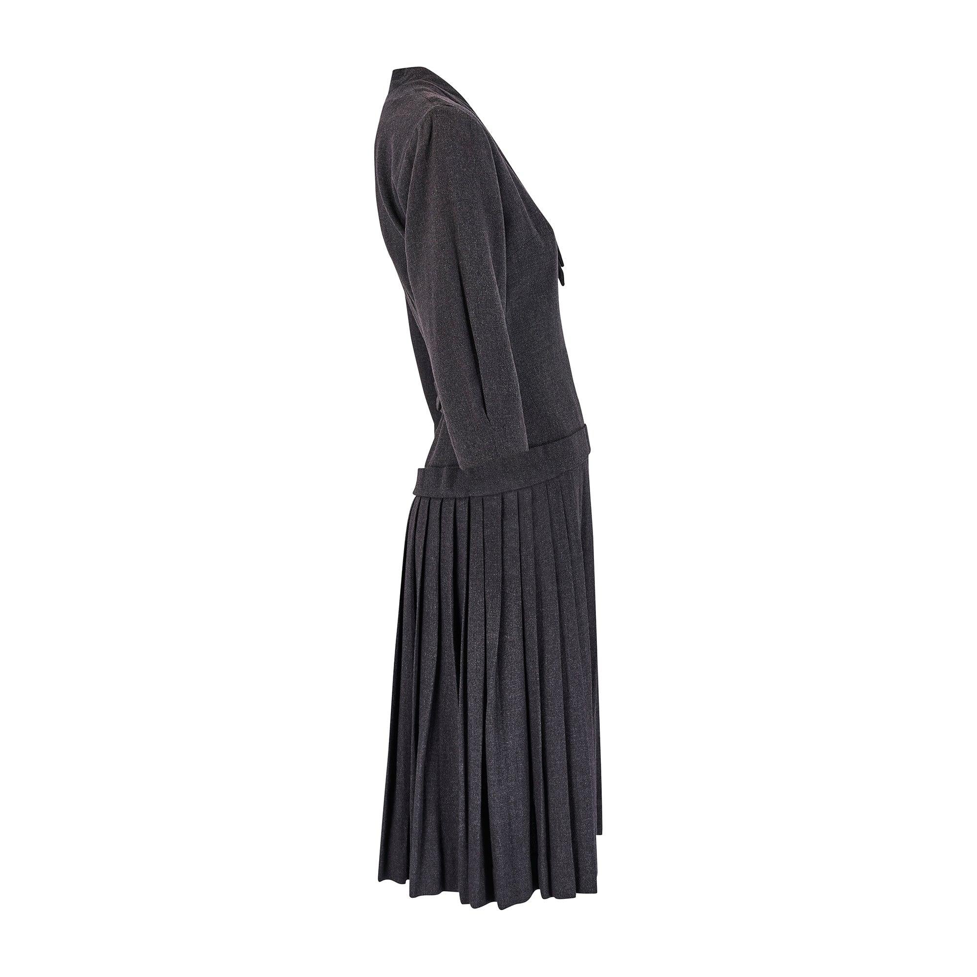 Questo abito dei primi anni '50 è di uno stilista sconosciuto, ma ricorda molto il New Look di Dior. Realizzato in lana leggera con finitura grigia screziata, presenta maniche a tre quarti e un'elegante scollatura a V, con due lacci sovrapposti che
