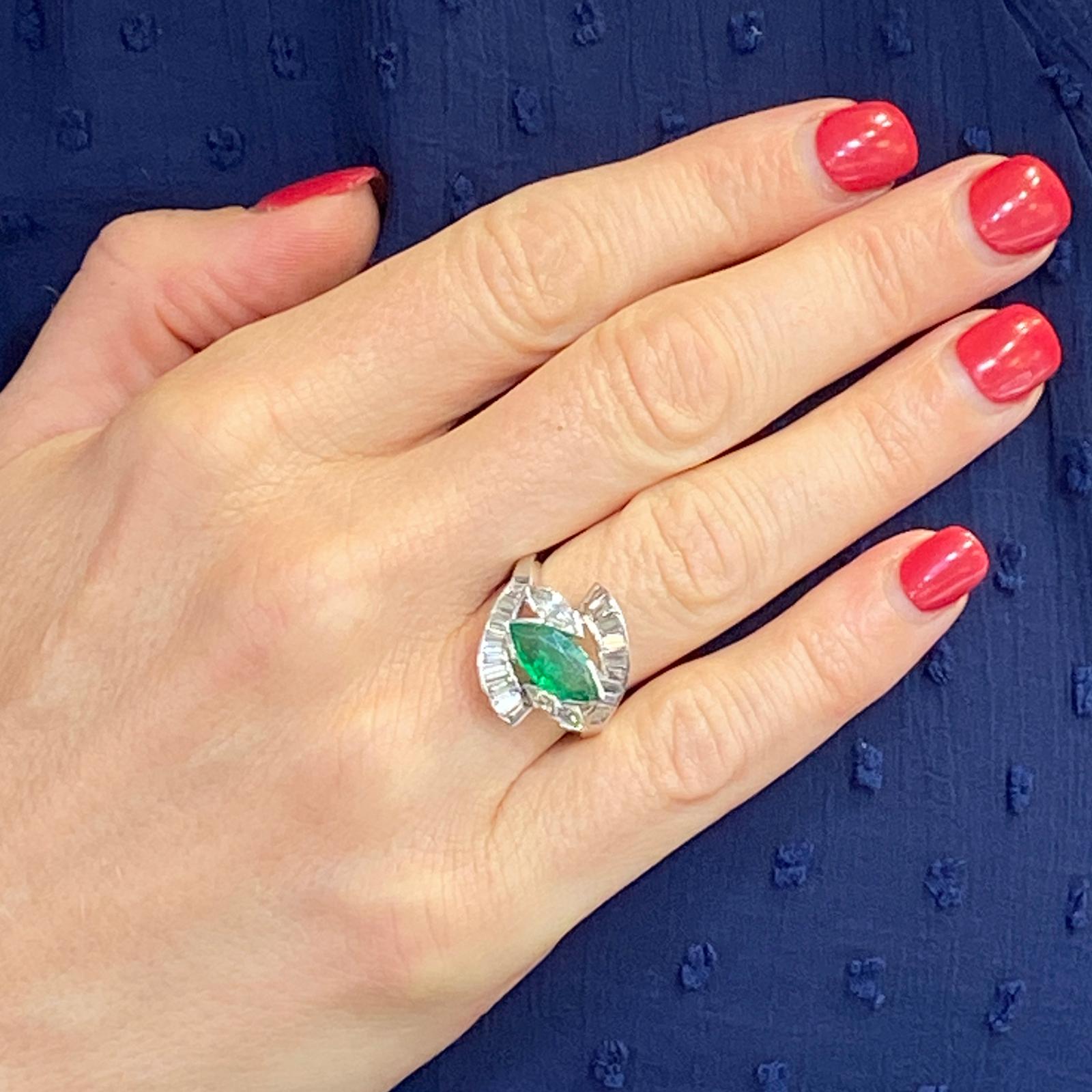 Handcrafted in platinum, this 1950's estate ring features an 1.50 carat marquise shape natural emerald gemstone surrounded by marquise and baguette cut diamonds. The diamonds weigh approximately 1.50 carat total weight. The ring is currently size