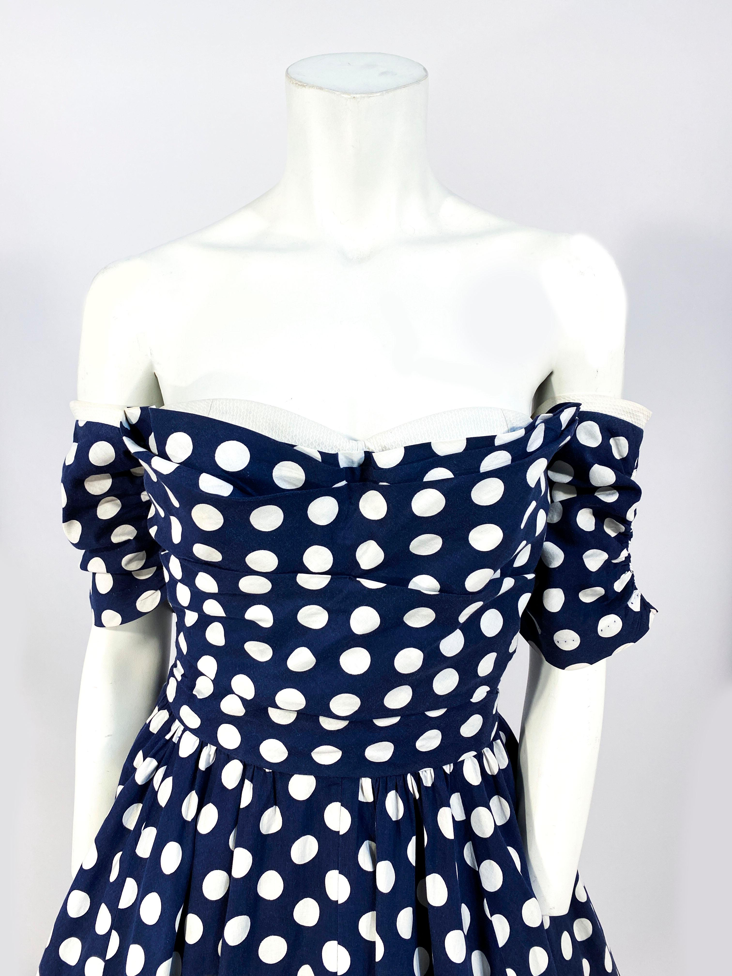 Early 1950s Navy and white polkadot summer party dress with removable off the shoulder sleeves to make this dress entirely strapless. The bodice is finished with a white pique panel to match this trim on the sleeves. The skirt is full and is