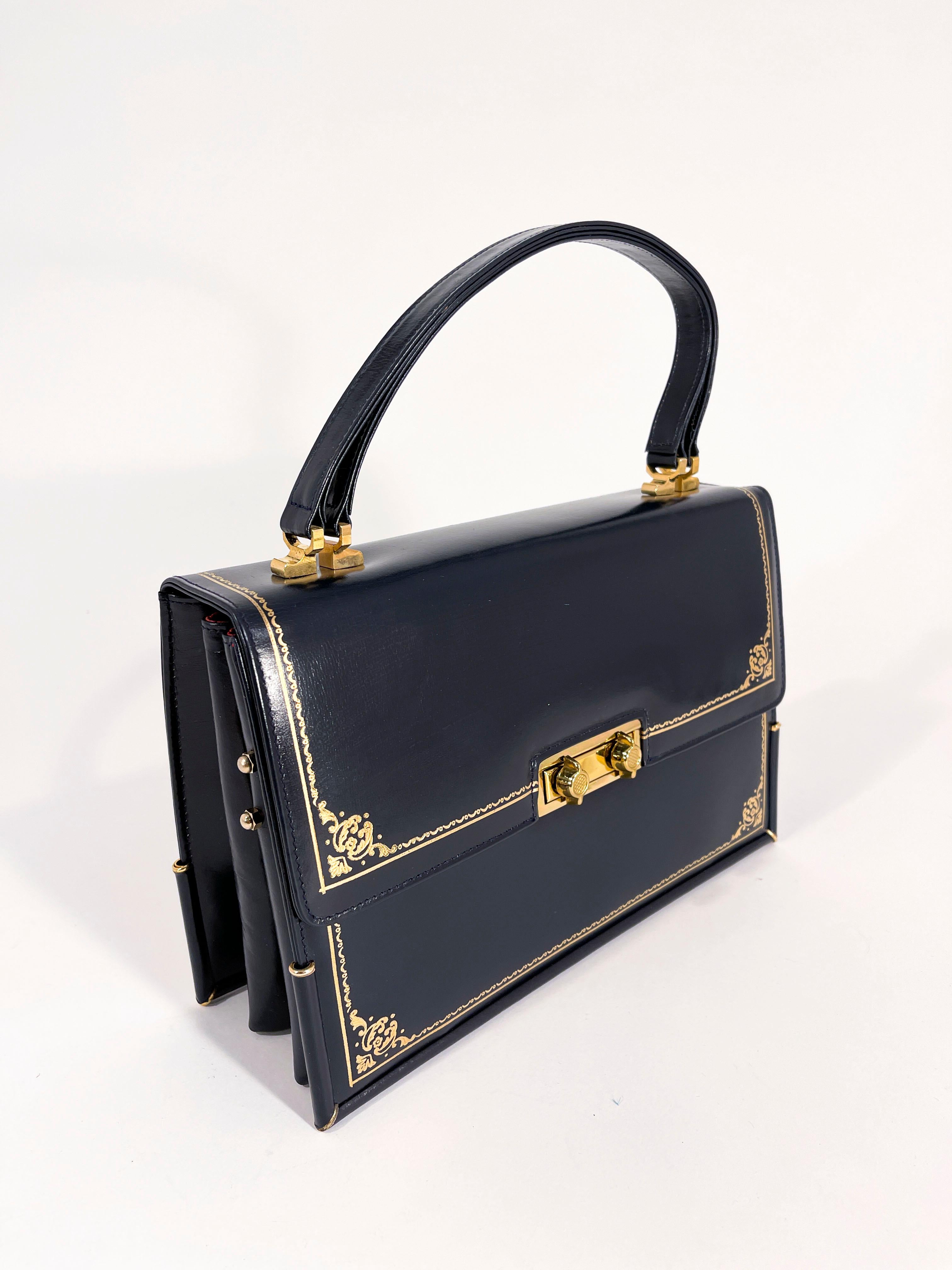 1950s Navy blue top-handle handbag featuring a book motif and shape. The front and back has gold embossing to mimic antique bound books. The entire purse has brass hardware including a double lock closure and reenforced brass edges to protect the