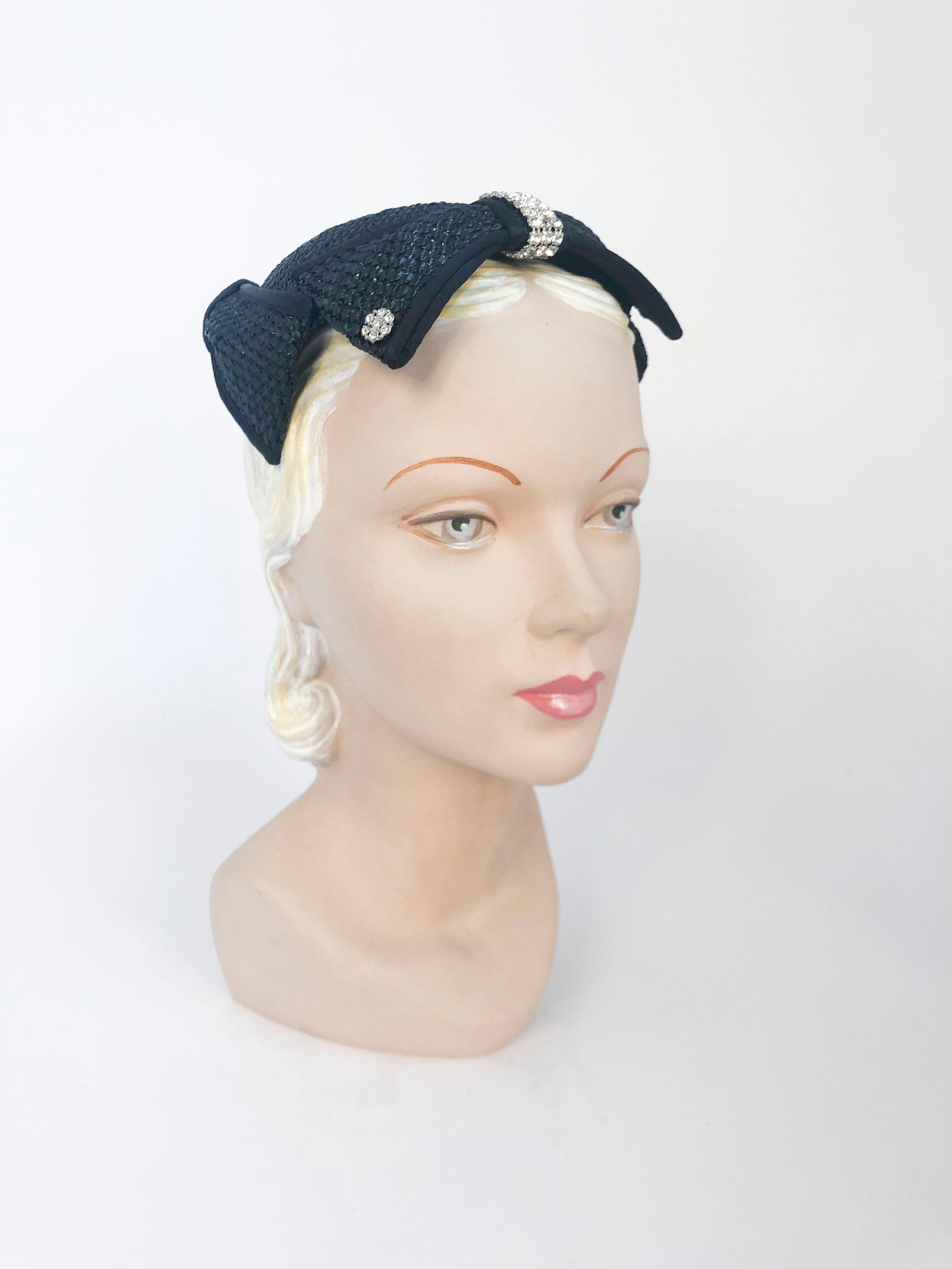 1950s Navy cocktail hat made of a woven raffia and is outlined in three oversized bows that are also trimmed with satin. The front bow has two rhinestone buttons, and a strip of rhinestone to accent the shape.