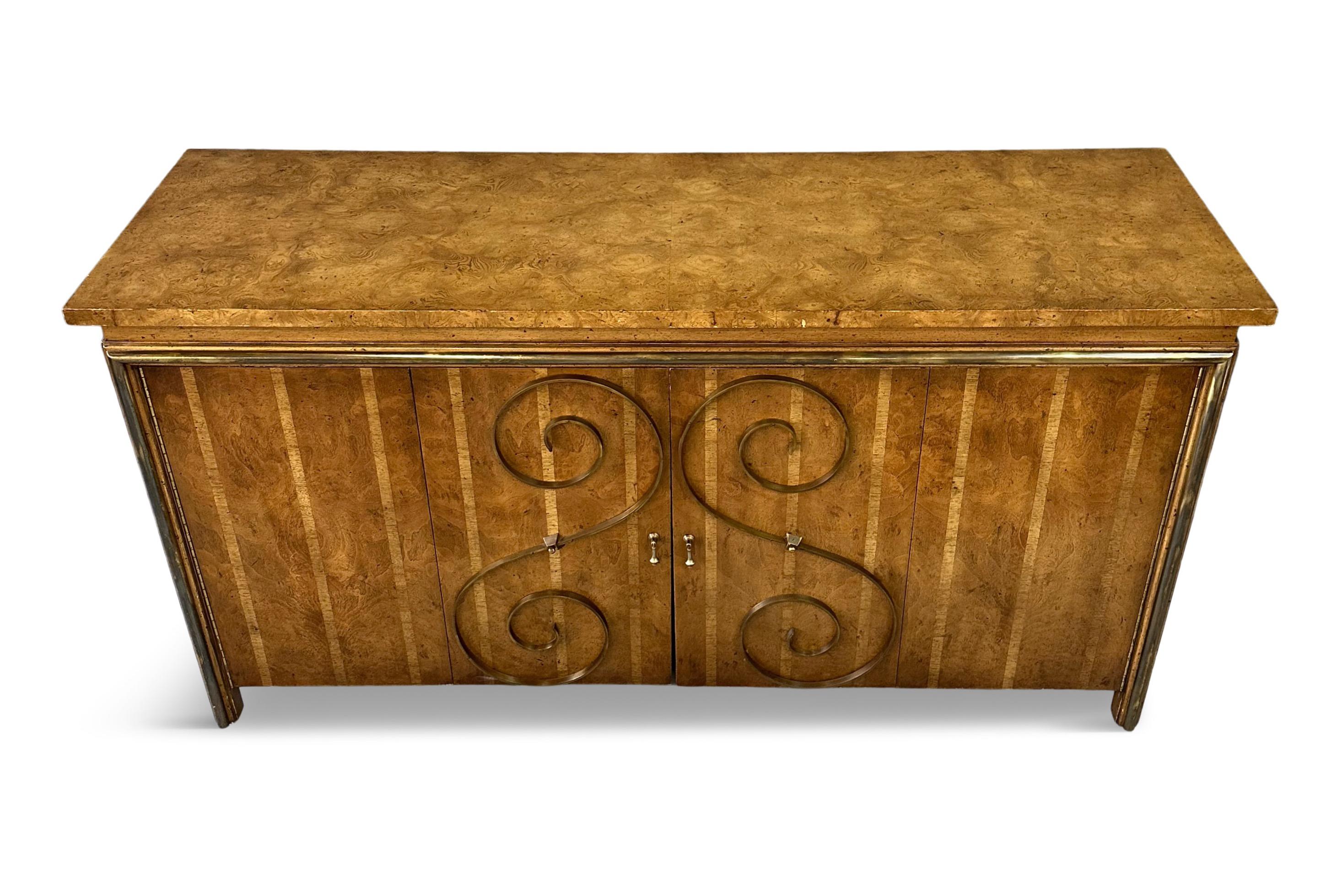 Lovely sideboard with four accordion doors in the Neoclassical style with a burl wood top and gracious brass scrolls decorating the doors. Inside you will find one side has a shelf and the other side has a drawer with silverware separations.