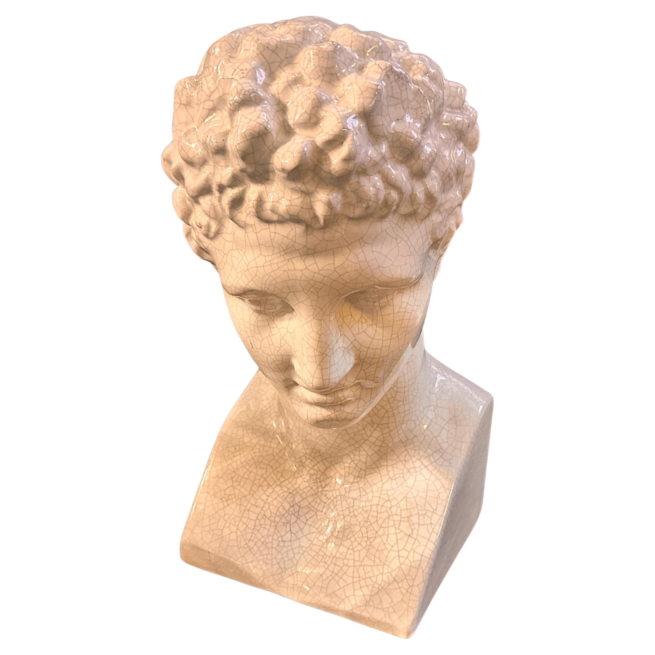 The image shows a Neoclassical ceramic bust of Antinoo (Antinous), a celebrated figure from classical antiquity. This particular bust, dating from the 1950s, is crafted in a white ceramic with a crackled finish, giving it an aged and textured