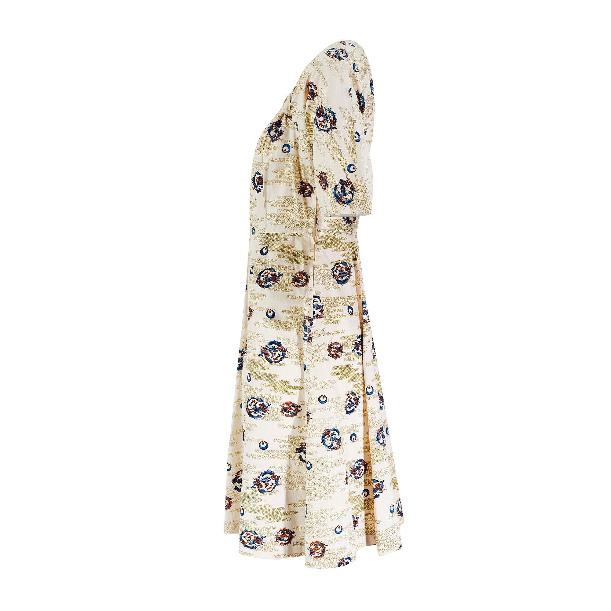 This 1950s cotton novelty print dress is tailored to a full-skirted, pleated style typical of this era. It has short-sleeves and a nipped-in waist. The square-neckline is held in place by gathered pieces of cotton in a pale chartreuse hue. The dress