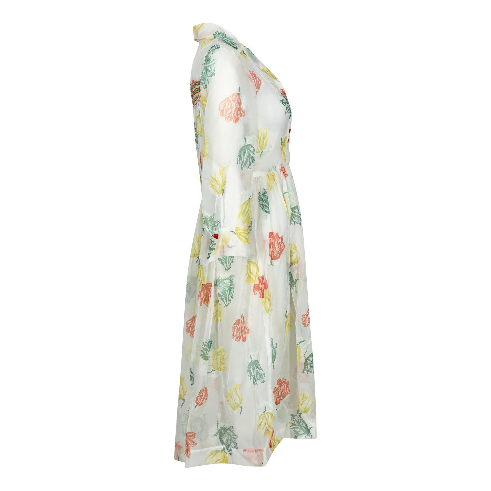 This is a really beautiful and original late 1950s or early 1960s organza floral print shirtwaister dress. The floral print, which we identify as tulips but could also be rose, is in mid-century colours of orange, green and yellow. The dress is a