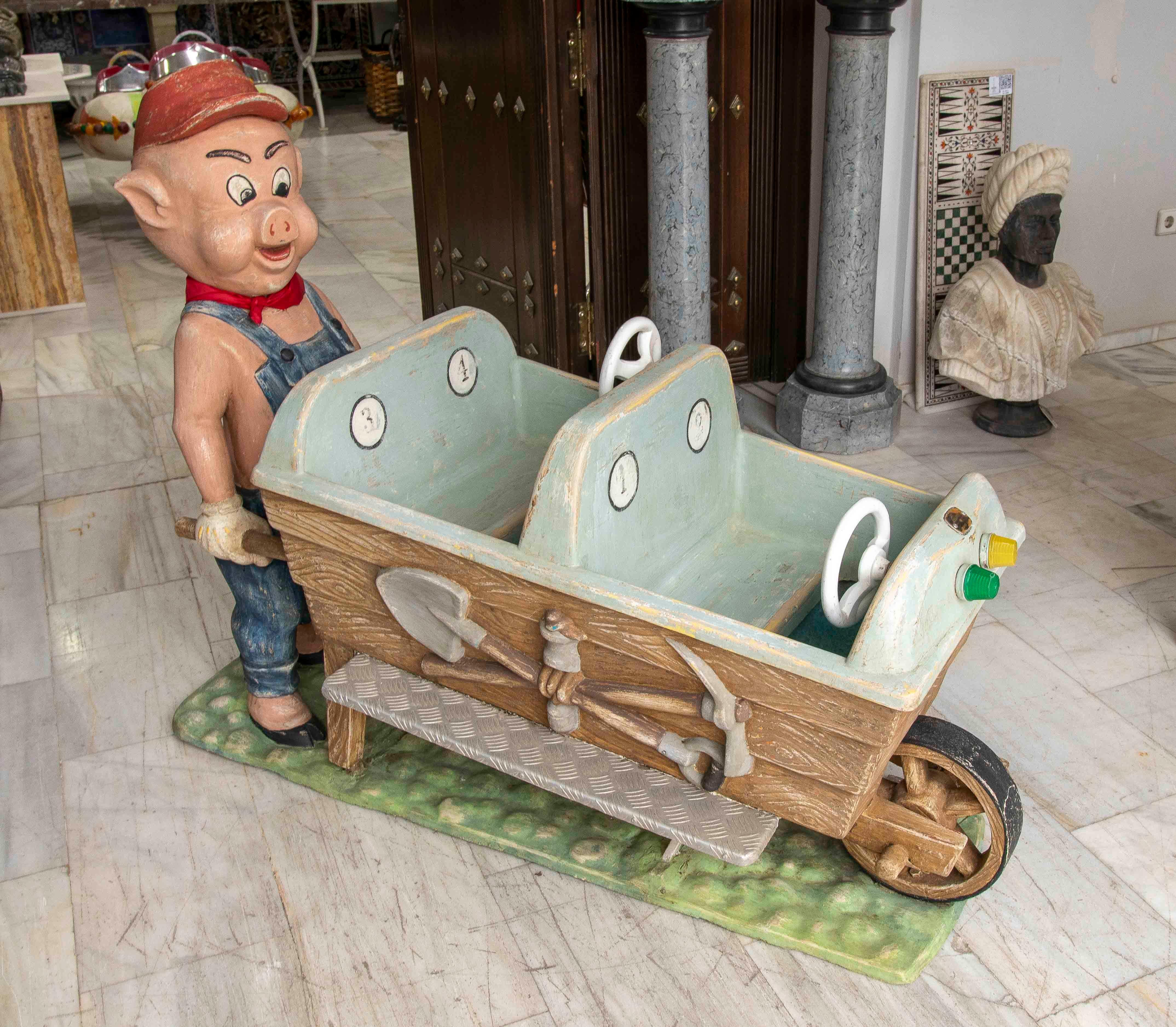 Incantevole giostra d'epoca per bambini decorata con una figura di maiale vestita da operaio della miniera che spinge un vagone a due piani per bambini. Il veicolo presenta due sedili dotati di piccoli volanti e indicatori decorativi, evocando