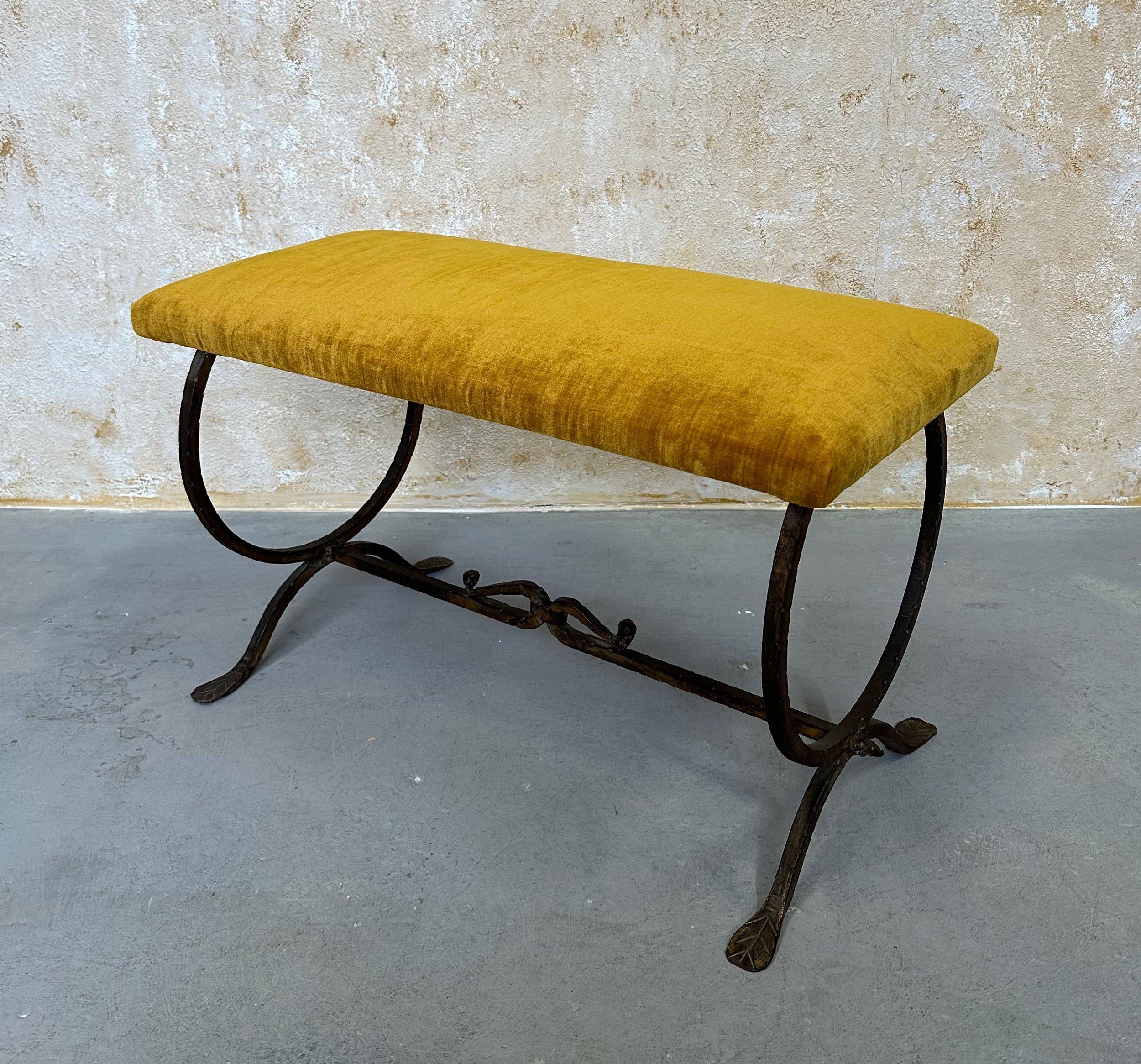 This lovely 1950s Spanish handwrought iron bench features an hourglass frame with a stretcher that has a central curled decorative detail and comes to a point at the ends. The frame is finished in a hand-applied dark gilt patina that contrasts the