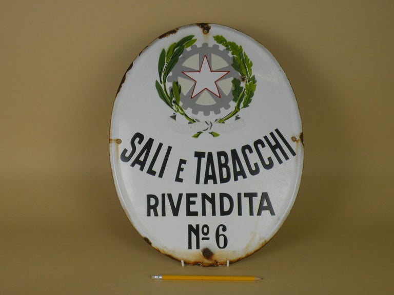 This vintage white enamel tobacco sign was used by small shops in Italy selling state-monopoly products such as tobacco and cigarettes but also salt and stamps.
This ‘Sali e Tabacchi’ oval sign with rounded edge is on white background and decorated