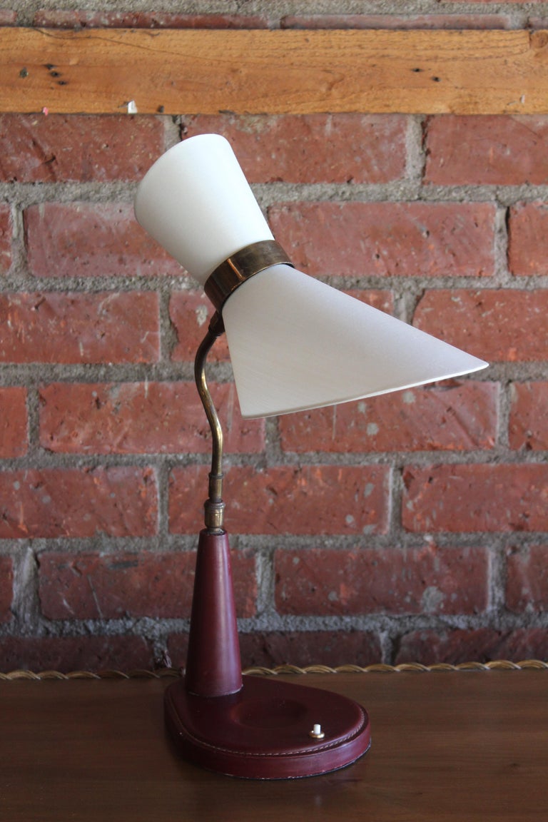 A vintage oxblood leather desk lamp by Jacques Adnet, France, 1950s. Restored with a new double cone silk shade to match the original. Newly rewired for U.S standards. Uses two candelabra bulbs.
