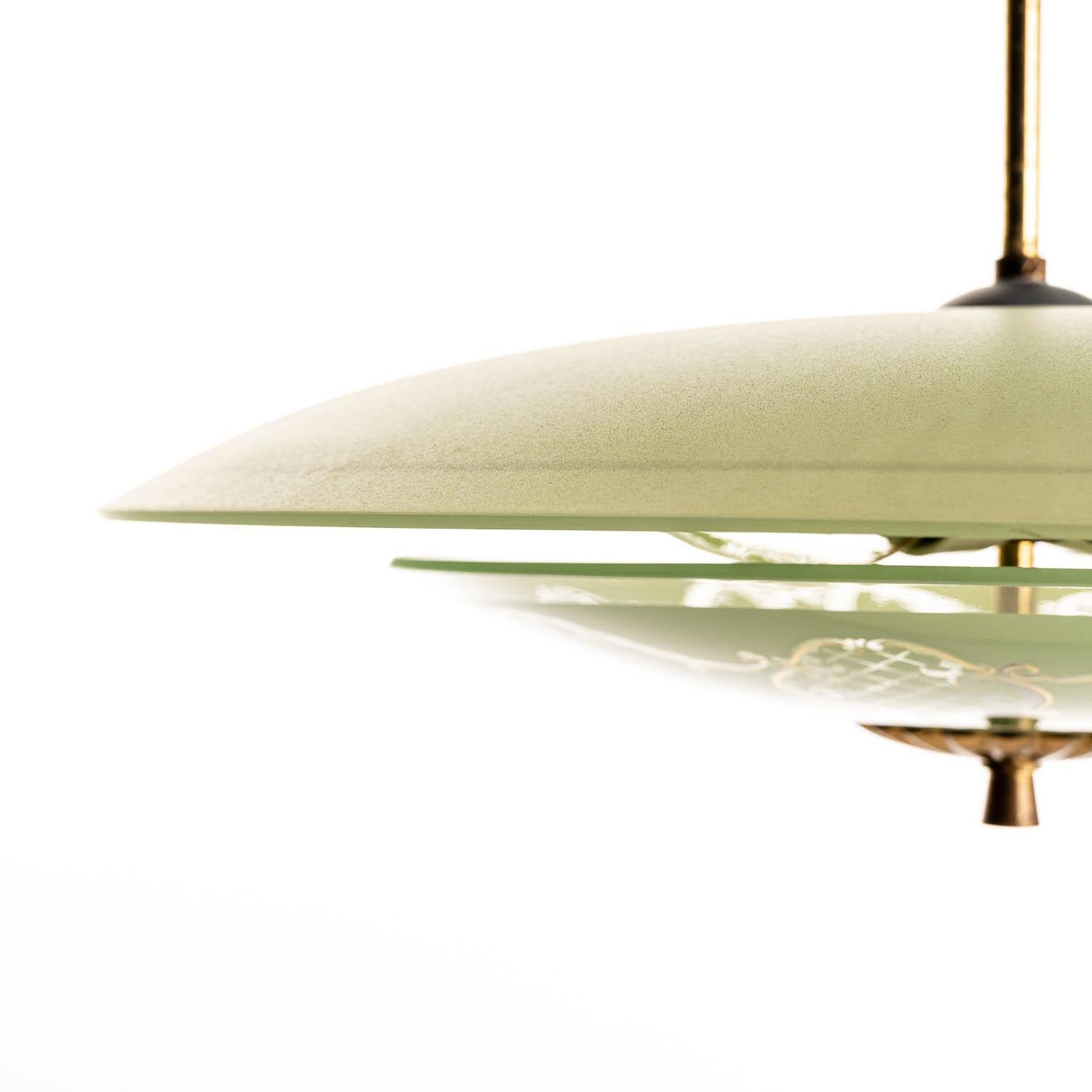 This elegant piece consisting of a brass frame and 2 unique frosted and satin glass reflectors. 
The lower round curved glass reflector with gold colored floral motifs on green glass saucer. Mounts below a round green glass with a gold colored