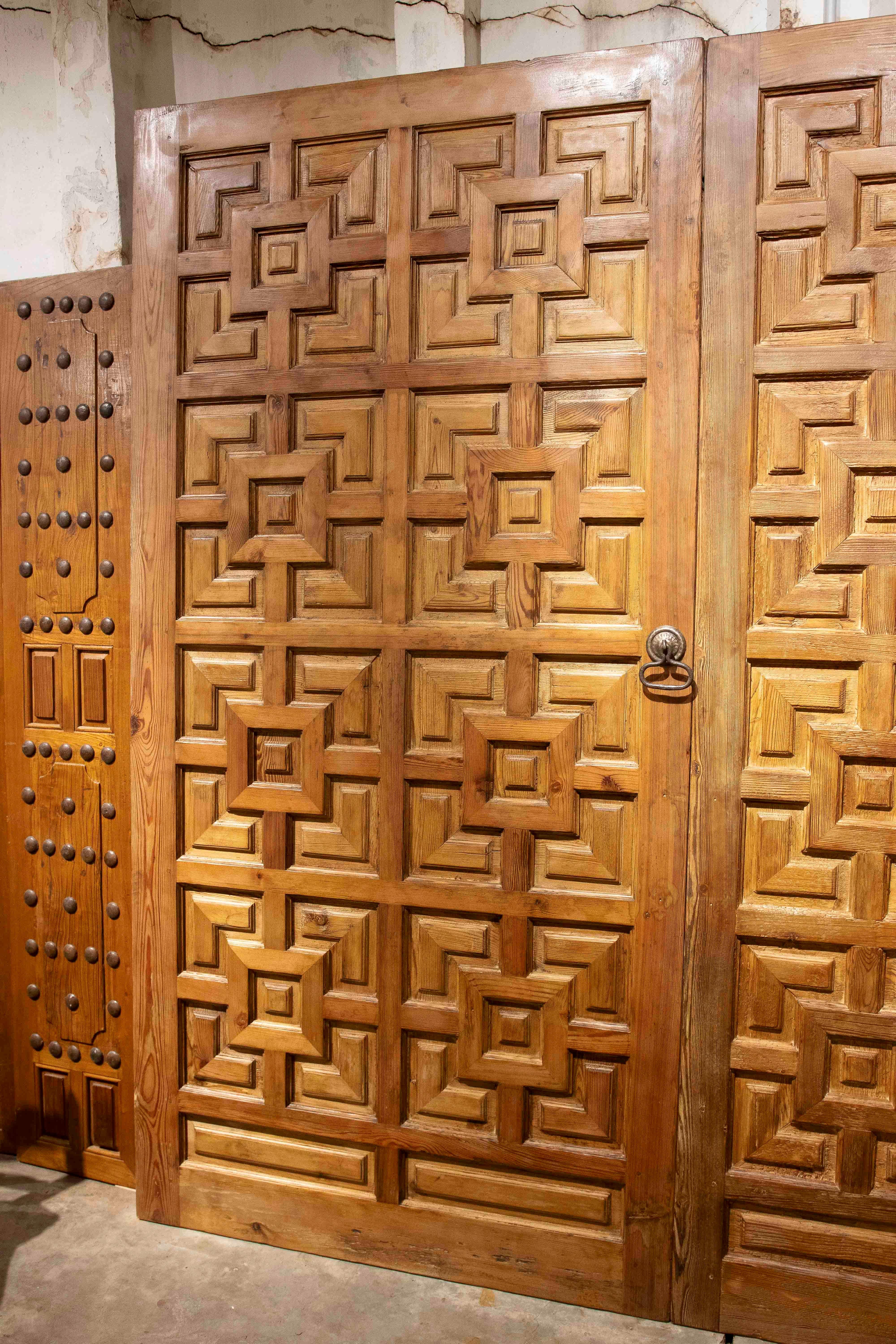 Une impressionnante paire de portes espagnoles anciennes, fabriquées en bois naturel massif, avec des sculptures géométriques en relief spectaculaires. Le design symétrique, basé sur des formes carrées et des losanges décalés, offre un fort impact