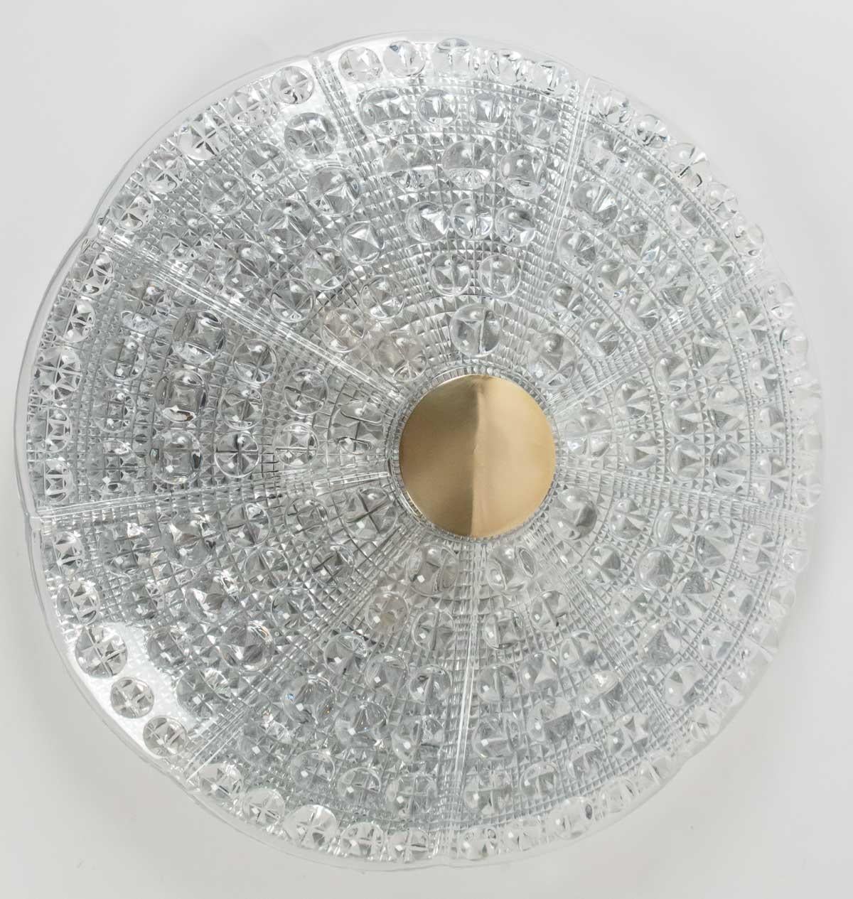 The shades of 40 centimeters of diameter are made of pressed glass with a pattern of blobs and facettes, adorned ay his center by a round piece of brass. 
Each light contain 6 bulbs.
Can be use as celling lights or sconces.
 