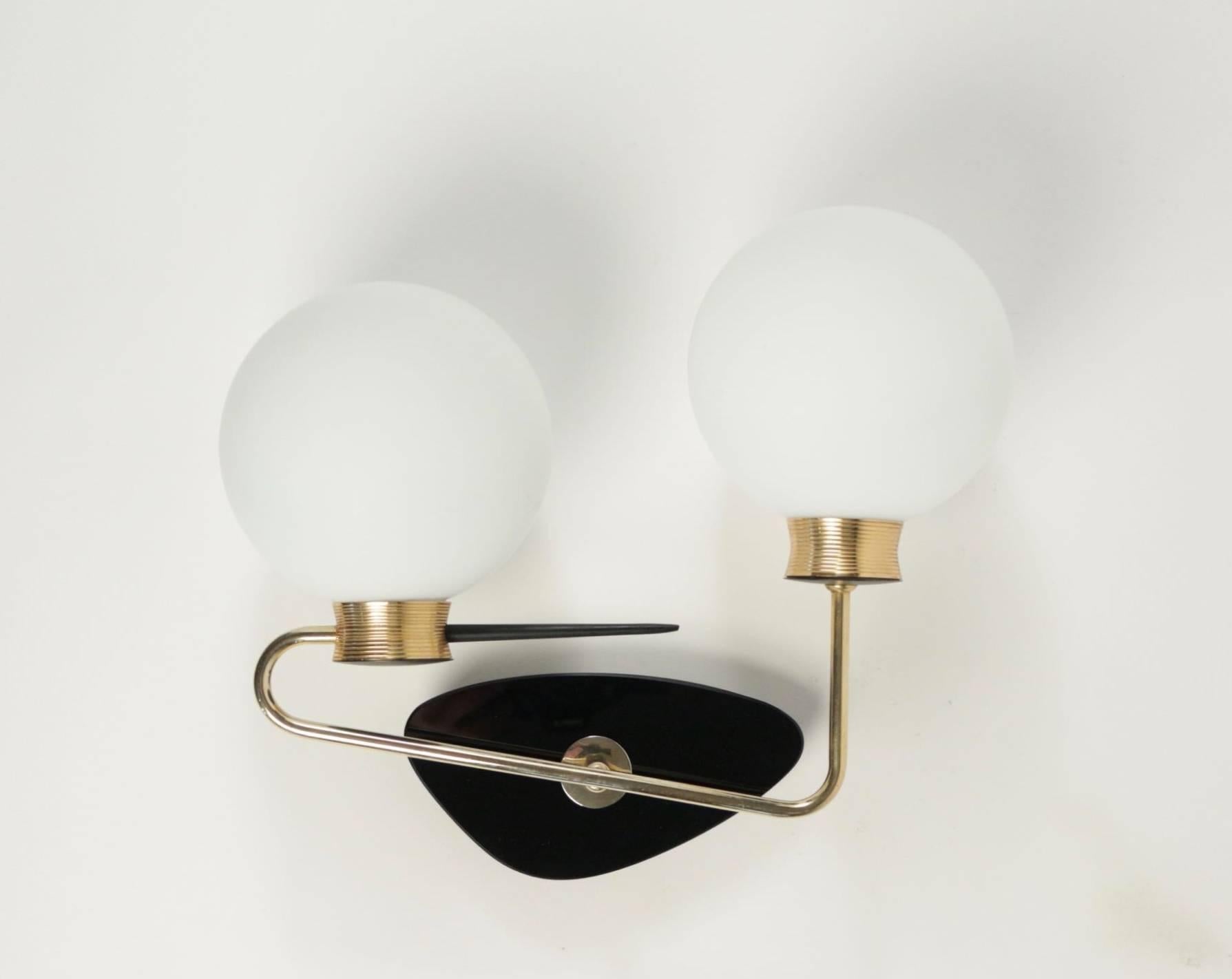 1950s pair of asymmetrical Arlus sconces. 

Ovoid shaped and black lacquered back plate.
Two round white satin glass lampshades mounted on curved brass arm ended by black stem.

Two bulbs per sconce.