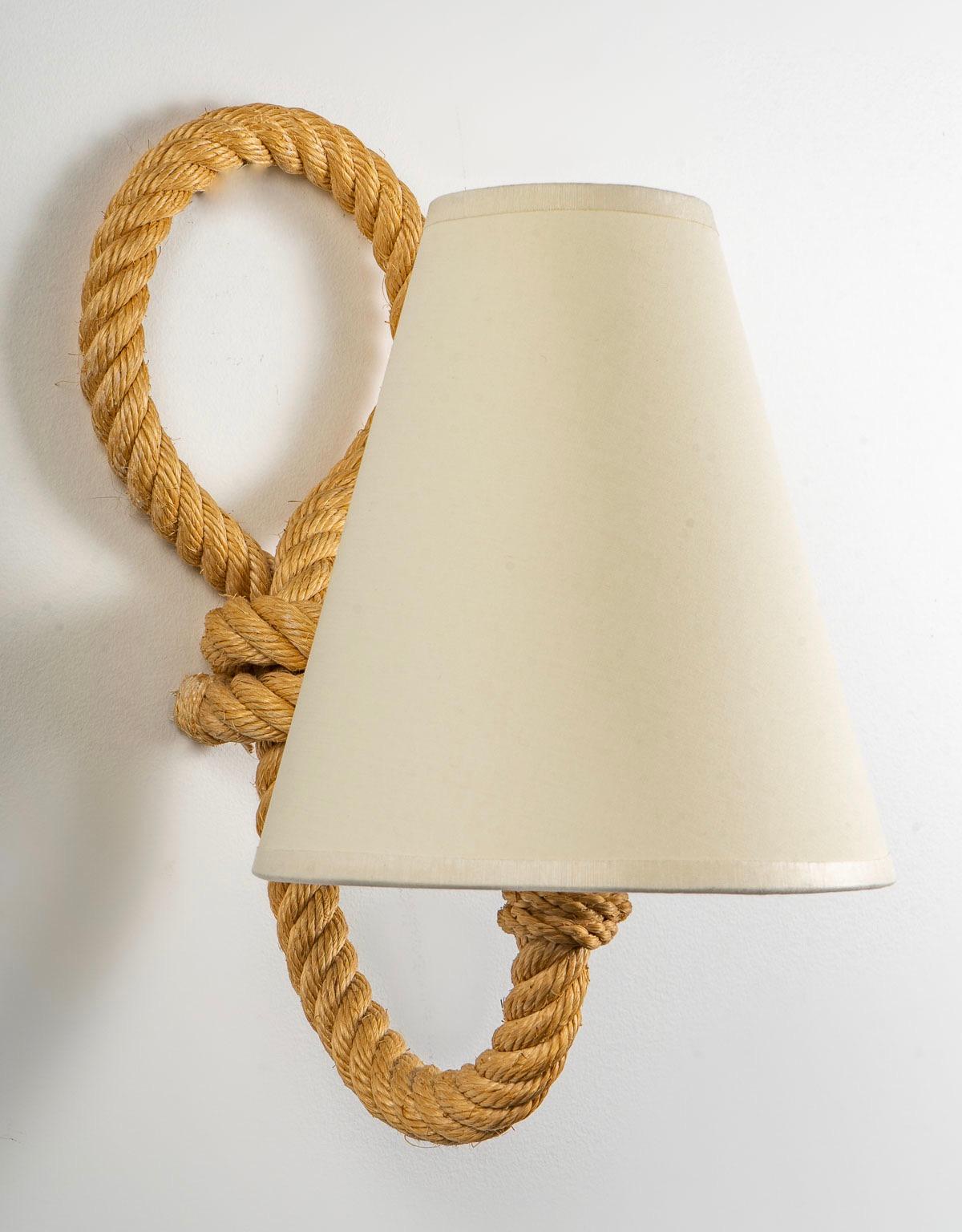 Each wall lamp is composed of a rope arm extending on the upper part to form a loop.
On the lower part, the arm of light returns towards the front, it is dressed with a lampshade in off-white cotton of trapezoidal form.
One bulb per wall