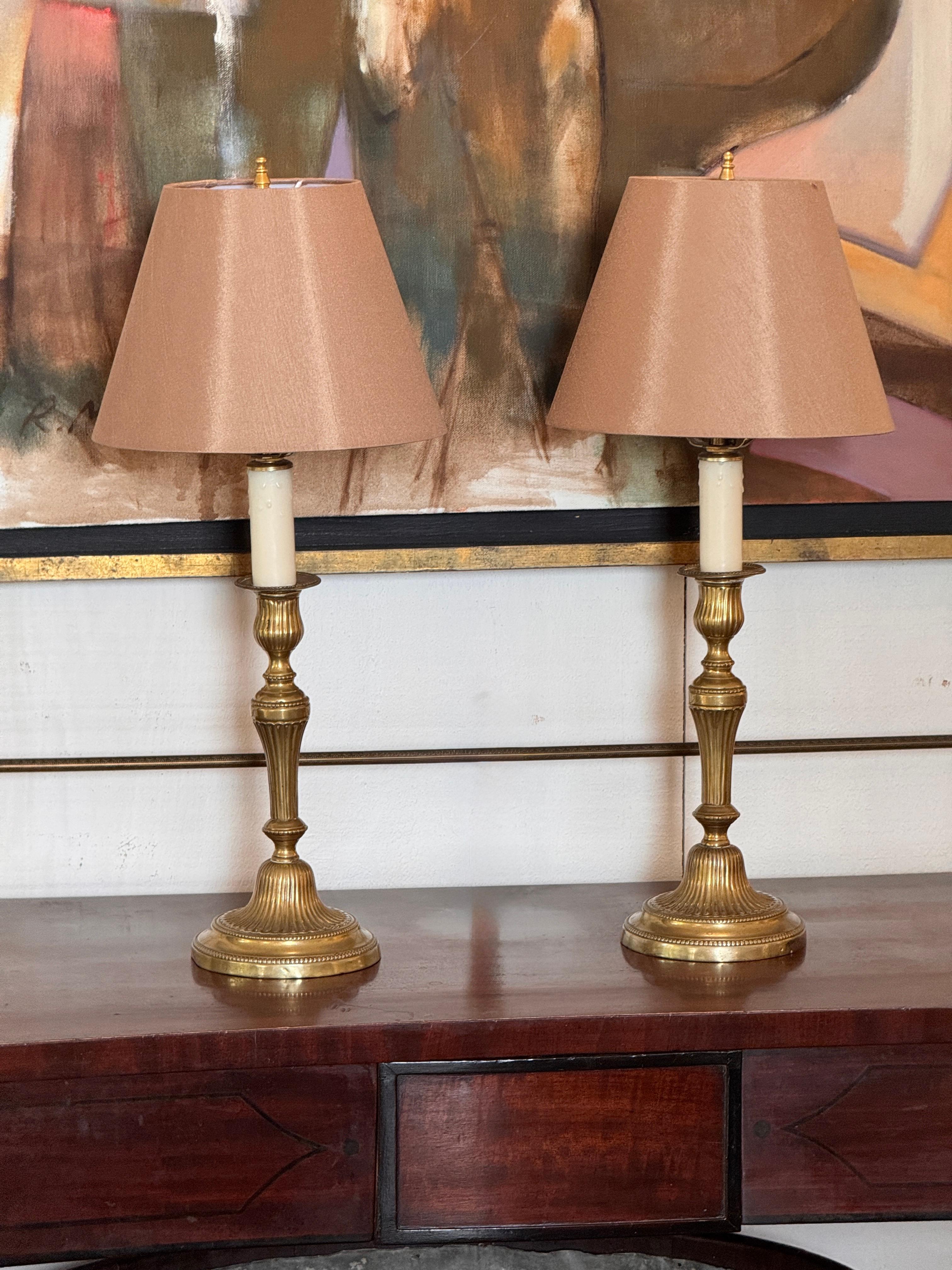 Chaque lampe a une forme de chandelier en laiton tourné et cannelé, reposant sur une base circulaire à gradins avec des détails perlés. Surface joliment vieillie avec une patine chaude.