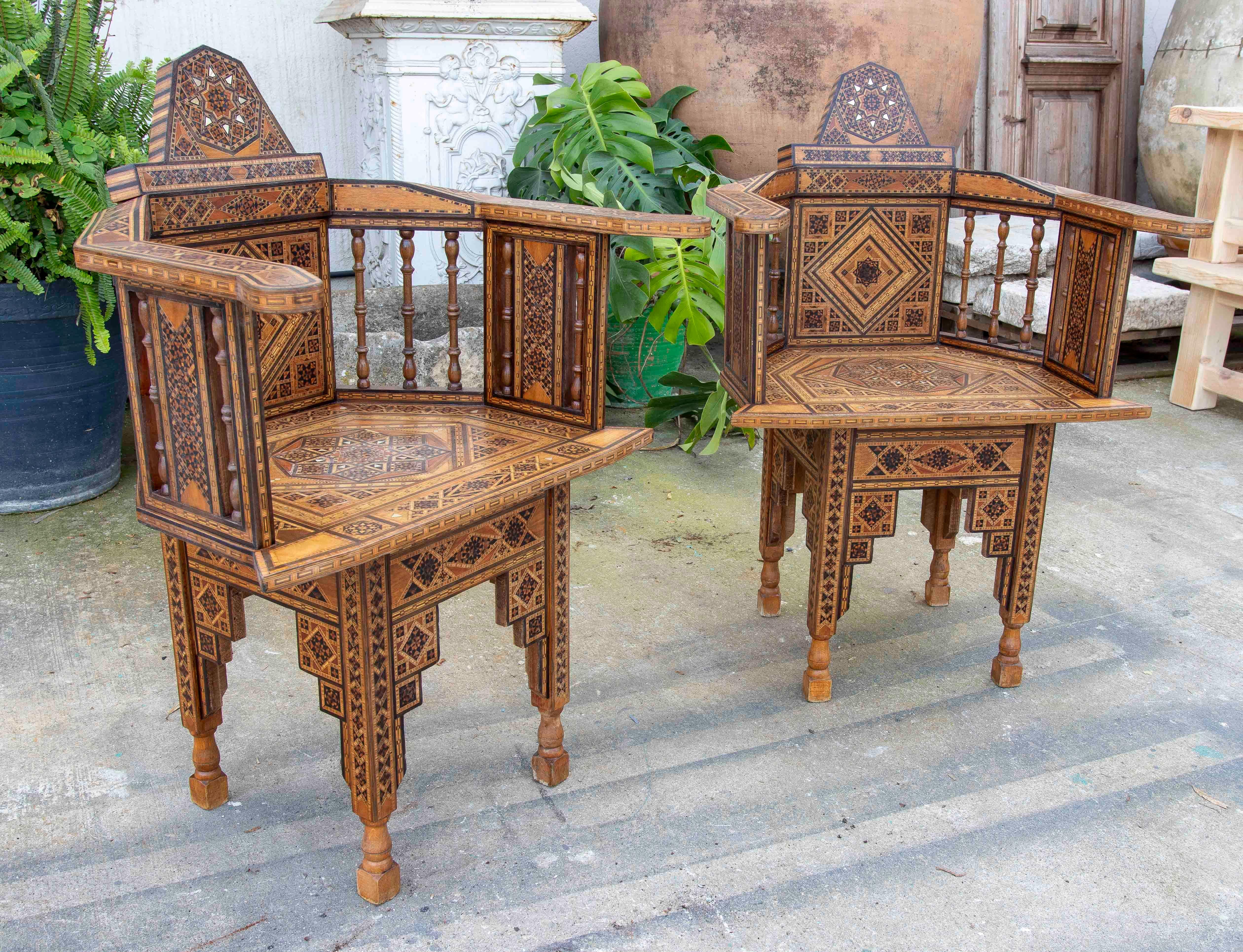 Bellissima coppia di sedie in legno con intricati dettagli intagliati e decorazioni geometriche intarsiate, che evocano uno stile arabo o mudéjar. Il suo design esagonale con braccioli e schienale alto evidenzia l'artigianato tradizionale, mentre i