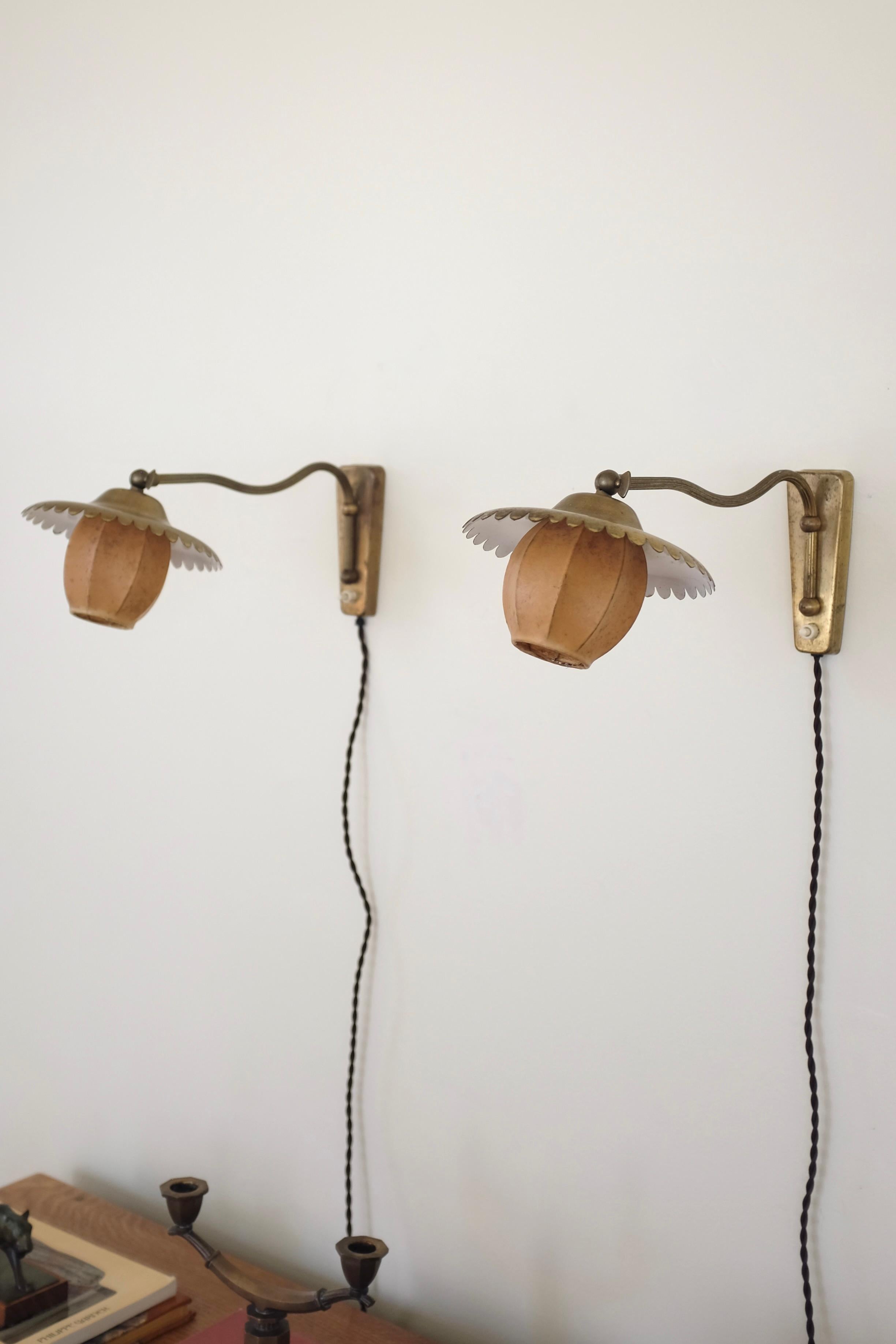 Charming Pair of 1950s Danish Wall lights attributed to Bent Karlby for Lyfa, Denmark. The lamps consist of a decorative brass lamp shade with a wavy edge and original sprayed plastic shades. The lamp arm has a soft curve and attach to the wall with