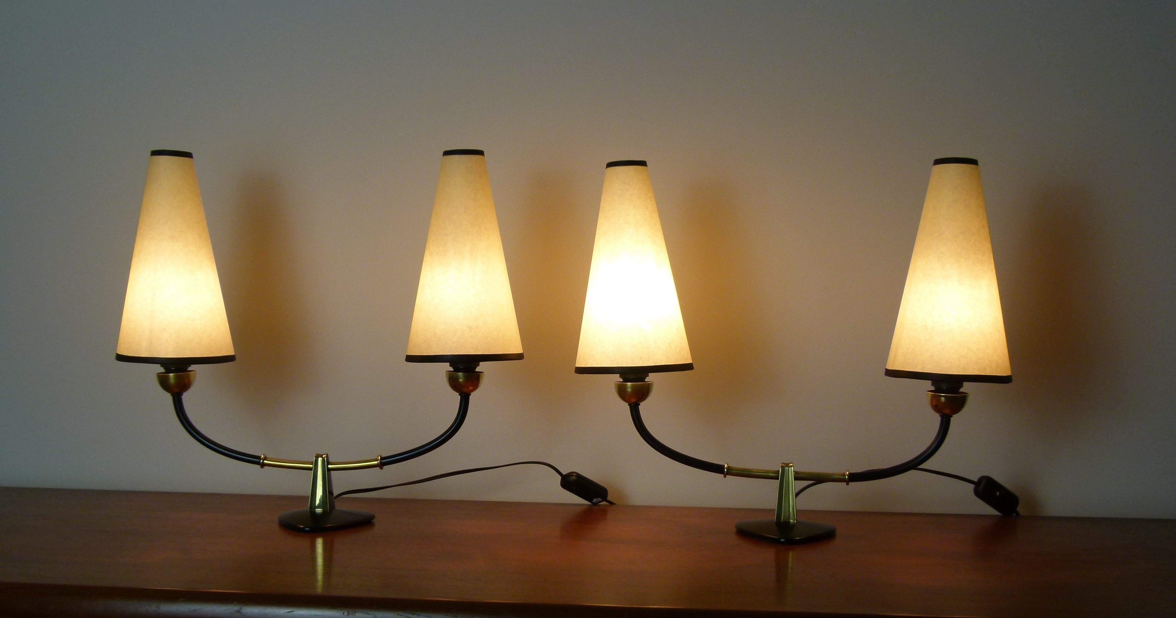 Pair of lamps with a double lampshade, composed of a triangular base in black lacquered metal, on which are set two arms of light in brass and black lacquered metal.
On each arm are placed a conical shaped lampshade with a black border.
These