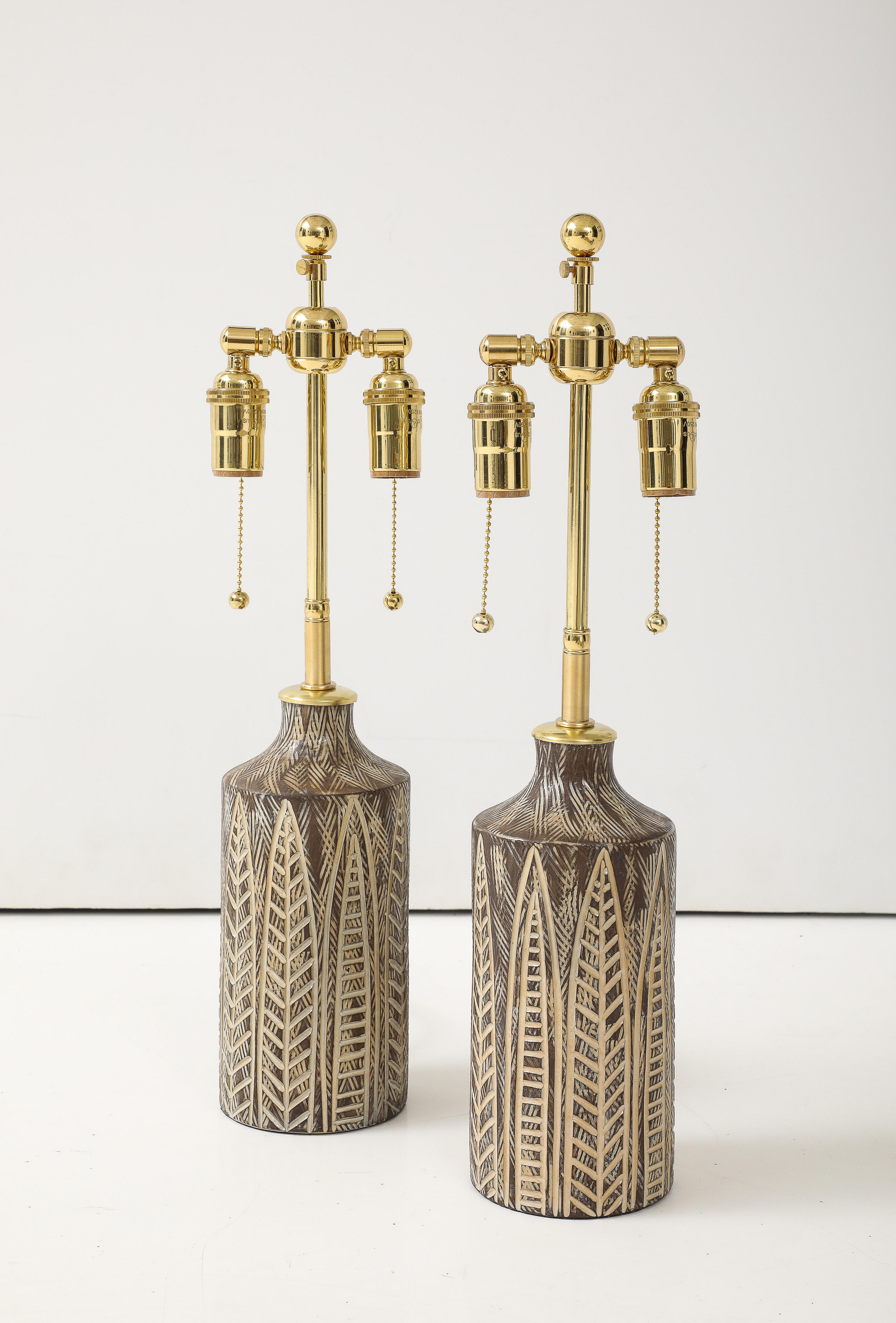 Wonderful pair of earth tone glazed ceramic table lamps with an incised leaf design.
The lamps have been Newly rewired for the US with adjustable polished brass double clusters and silk rayon cords.
Each socket takes standard size light bulbs with a