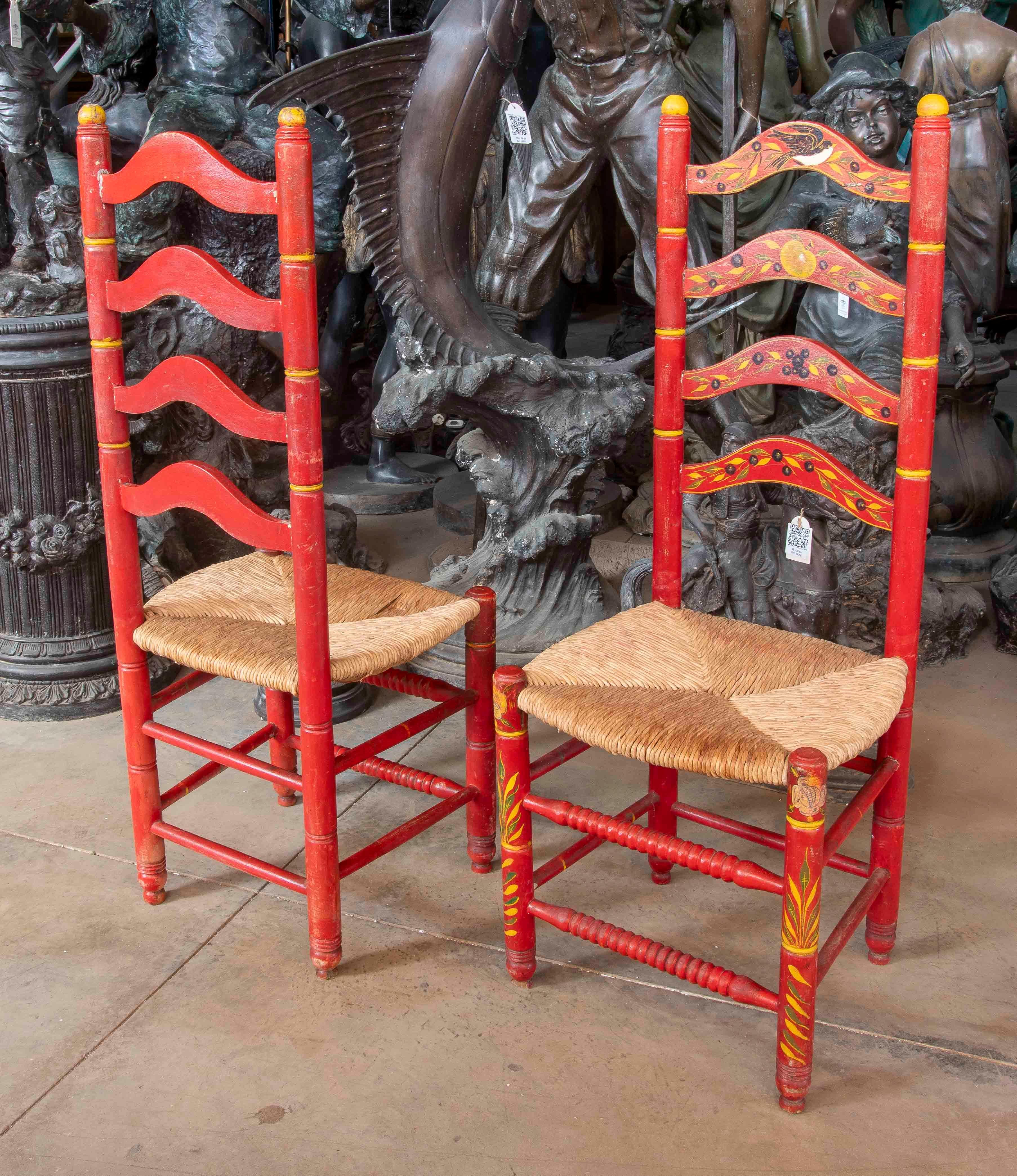 Un'affascinante coppia di sedie rustiche spagnole con strutture in legno massiccio dipinte a mano in un vibrante rosso con dettagli floreali e geometrici nei toni del giallo e del nero. Questi pezzi evocano lo stile tradizionale andaluso, fondendo