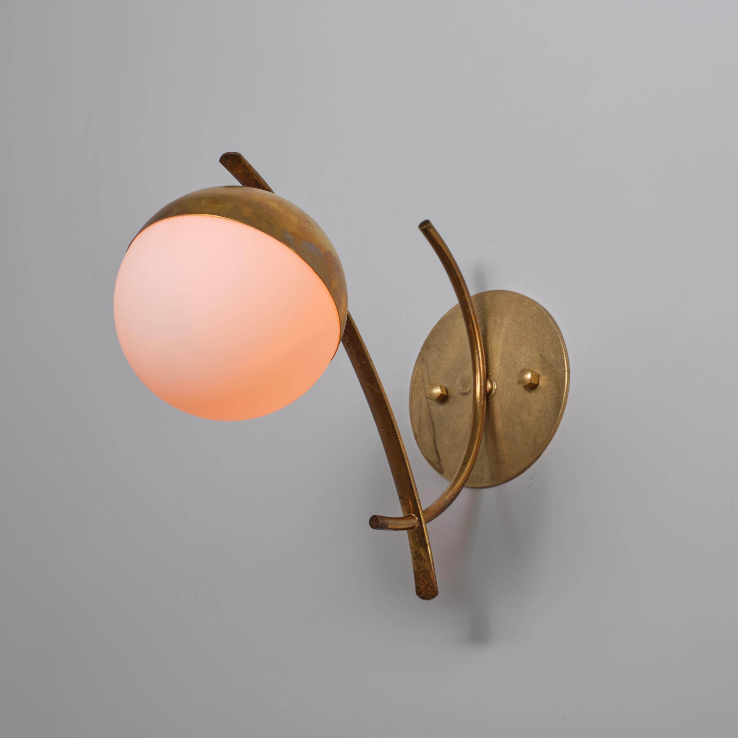 Coppia di appliques italiane degli anni '50, caratterizzate da una scultorea struttura in ottone con bracci curvi che sostengono diffusori sferici in vetro opalino. L'ottone presenta attraenti segni di ossidazione sviluppati nel tempo, che esaltano