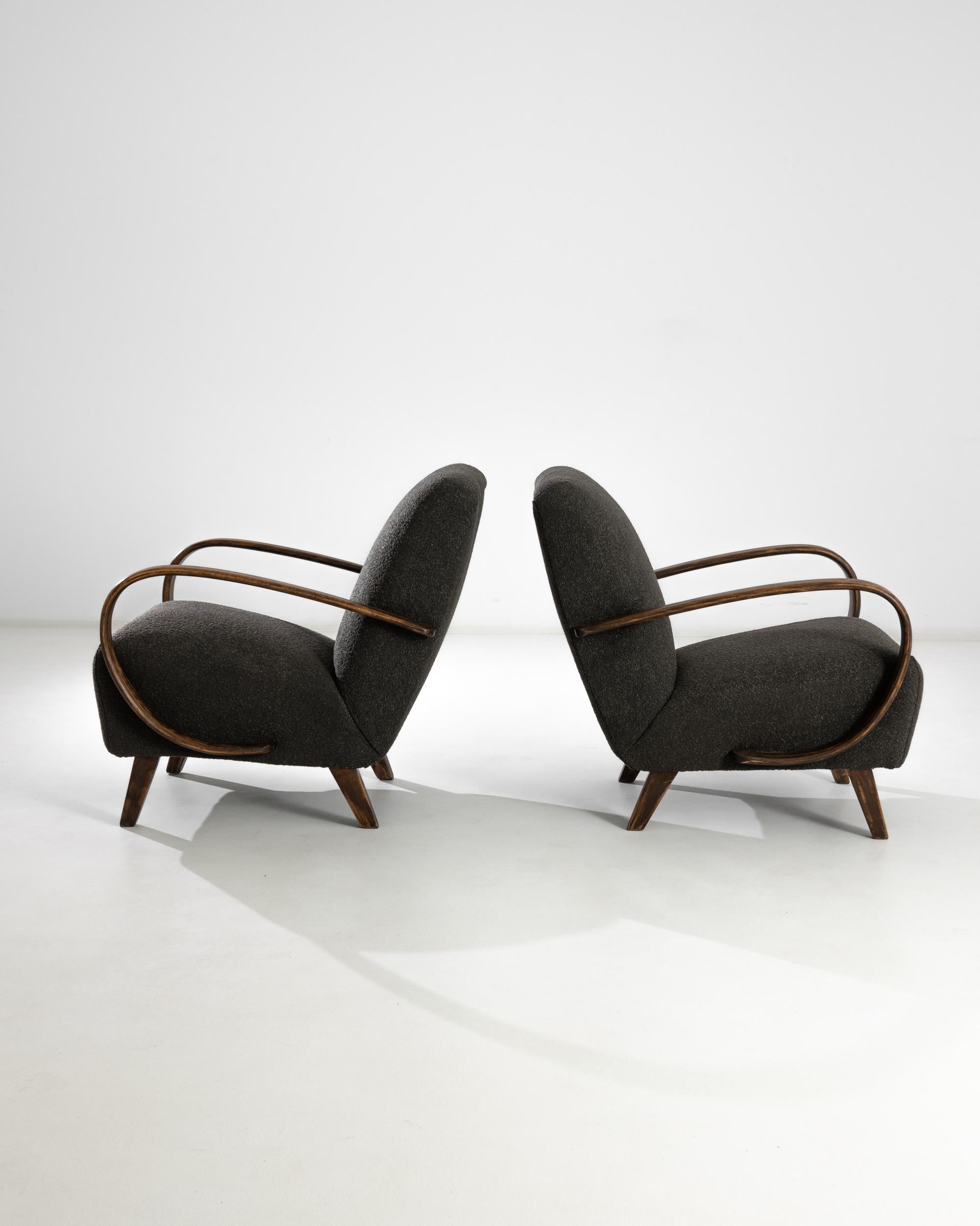 A design originally conceived in the 1930s by iconic Czech industrial designer J. Halabala, this vintage pair was realized circa 1950. A pair of swooping bentwood armrests frame a generous cushioned seat, upholstered in charcoal grey boucle. The