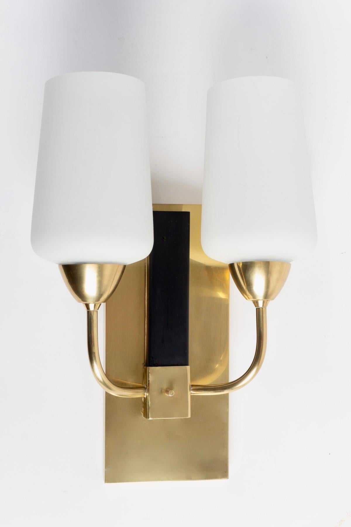 Pair of Maison Lunel wall lights from the 1950s,

Composed of a large wall plate in gilded brass on which are positioned two sconces formed by two rising rods, they are dressed in satin opal glass.
A small blackened brass plaque placed on the wall