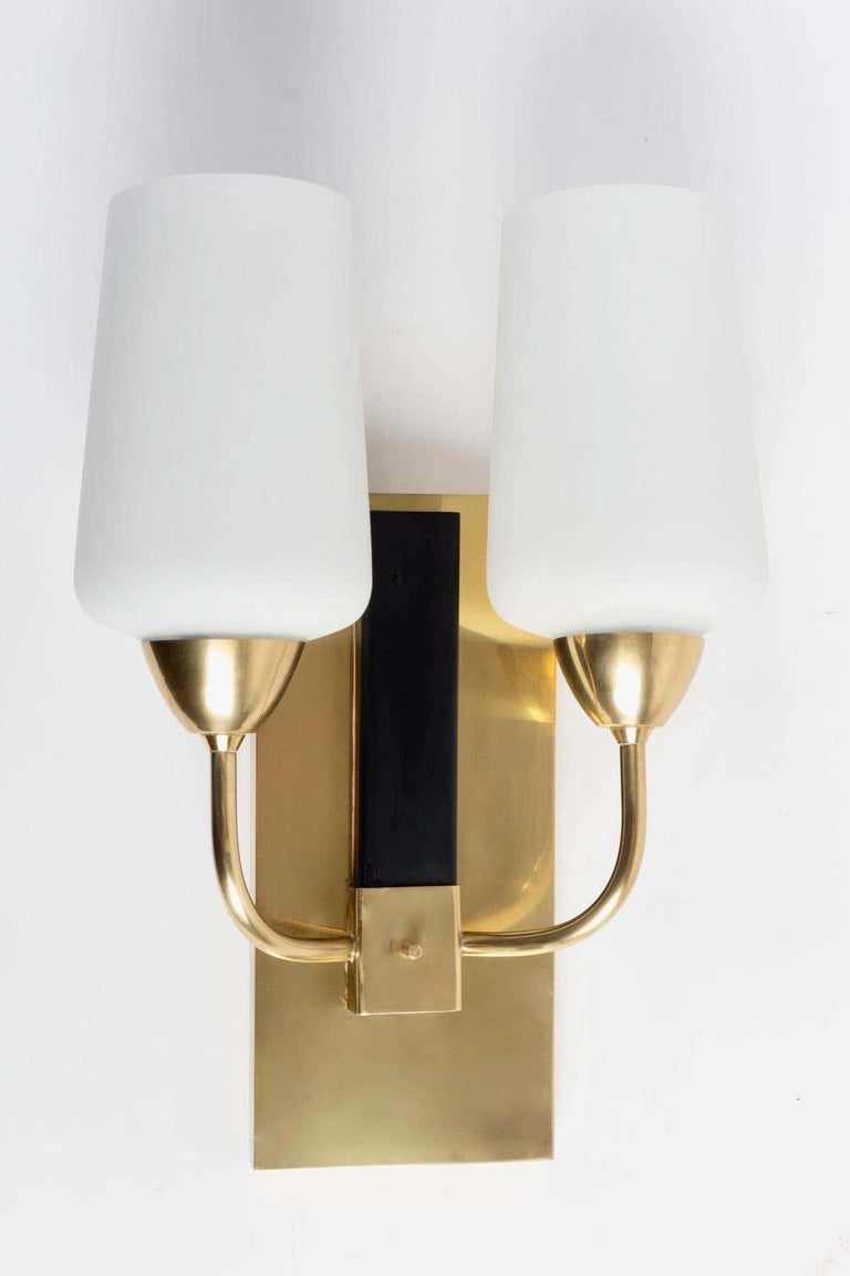 Pair of Maison Lunel wall lights from the 1950s,

Composed of a large wall plate in gilded brass on which are positioned two sconces formed by two rising rods, they are dressed in satin opal glass.
A small blackened brass plaque placed on the