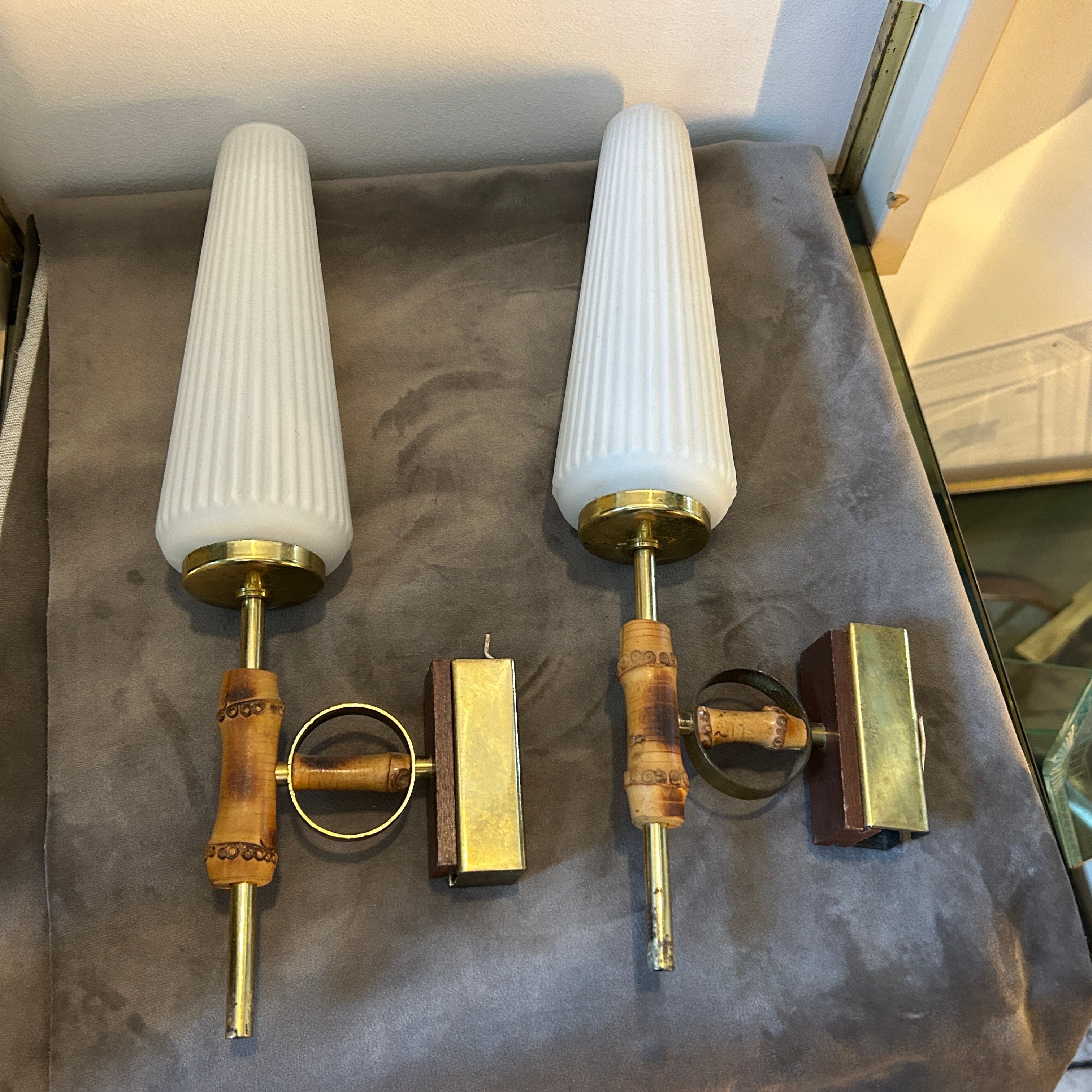 Two Mid-Century Modern brass, white glass and fake bamboo wood wall sconces designed and manufactured in Italy in the Fifties in very good conditions and in working order. The sconces feature a sleek and modern design, with brass and wood elements