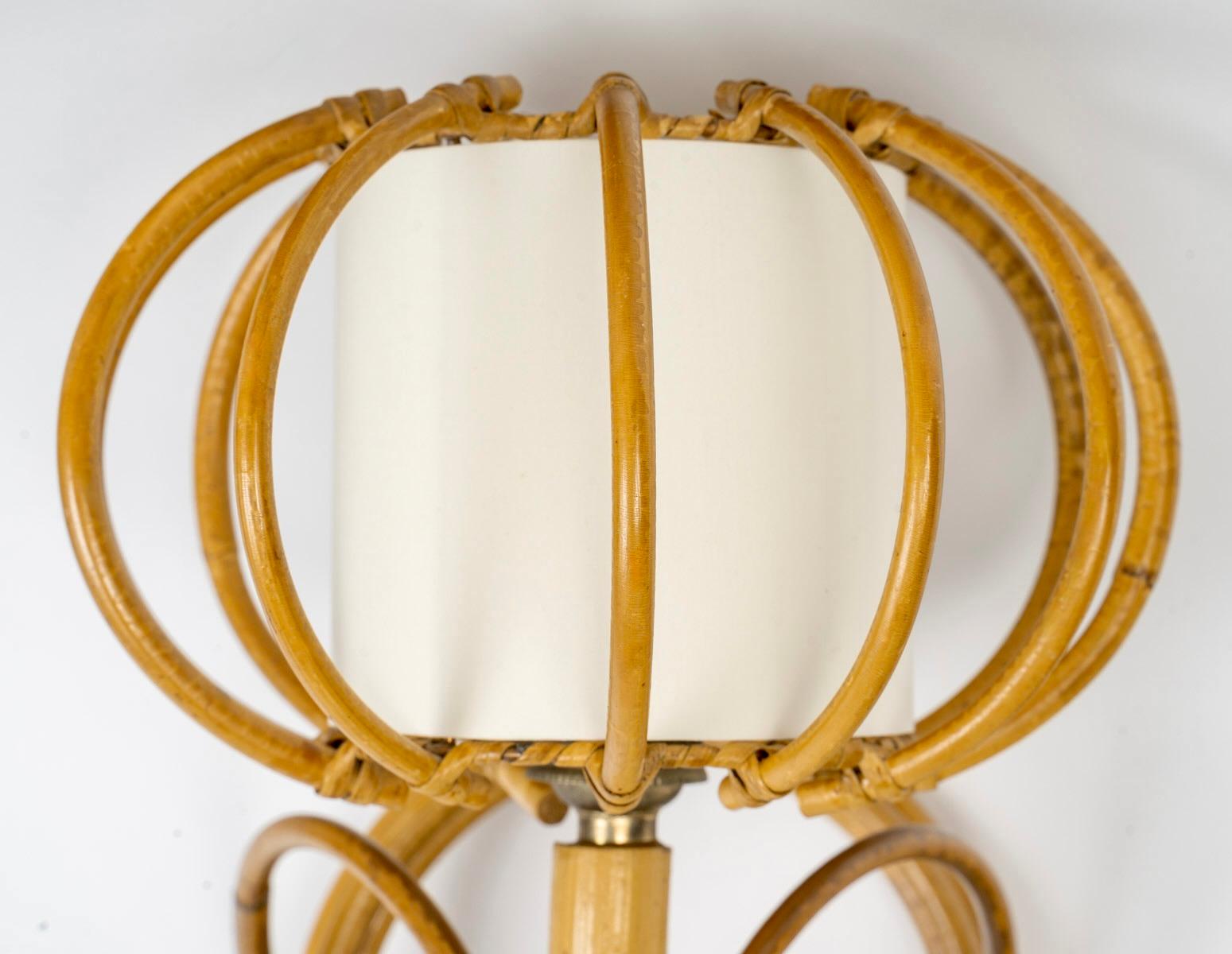 1950s, pair of rattan sconces to Louis Sognot.
Composed of a base formed by a bamboo stem forming a circle on which is positioned on the lower part a curved bamboo stem rising maintained by two small bamboo stems. 
The wall lamp is dressed with a