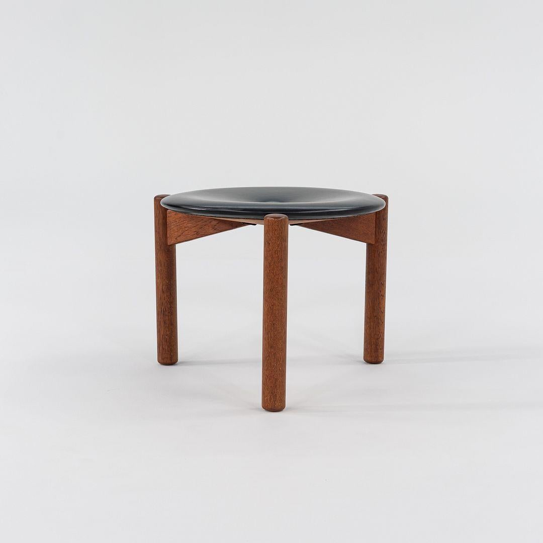 This is a pair of low three-legged stools, designed by Uno & Osten Kristiansson for Luxus of Sweden in the 1950s. The listed price includes the pair of stools as shown. Their design includes a round upholstered seat in black vinyl or leather, while