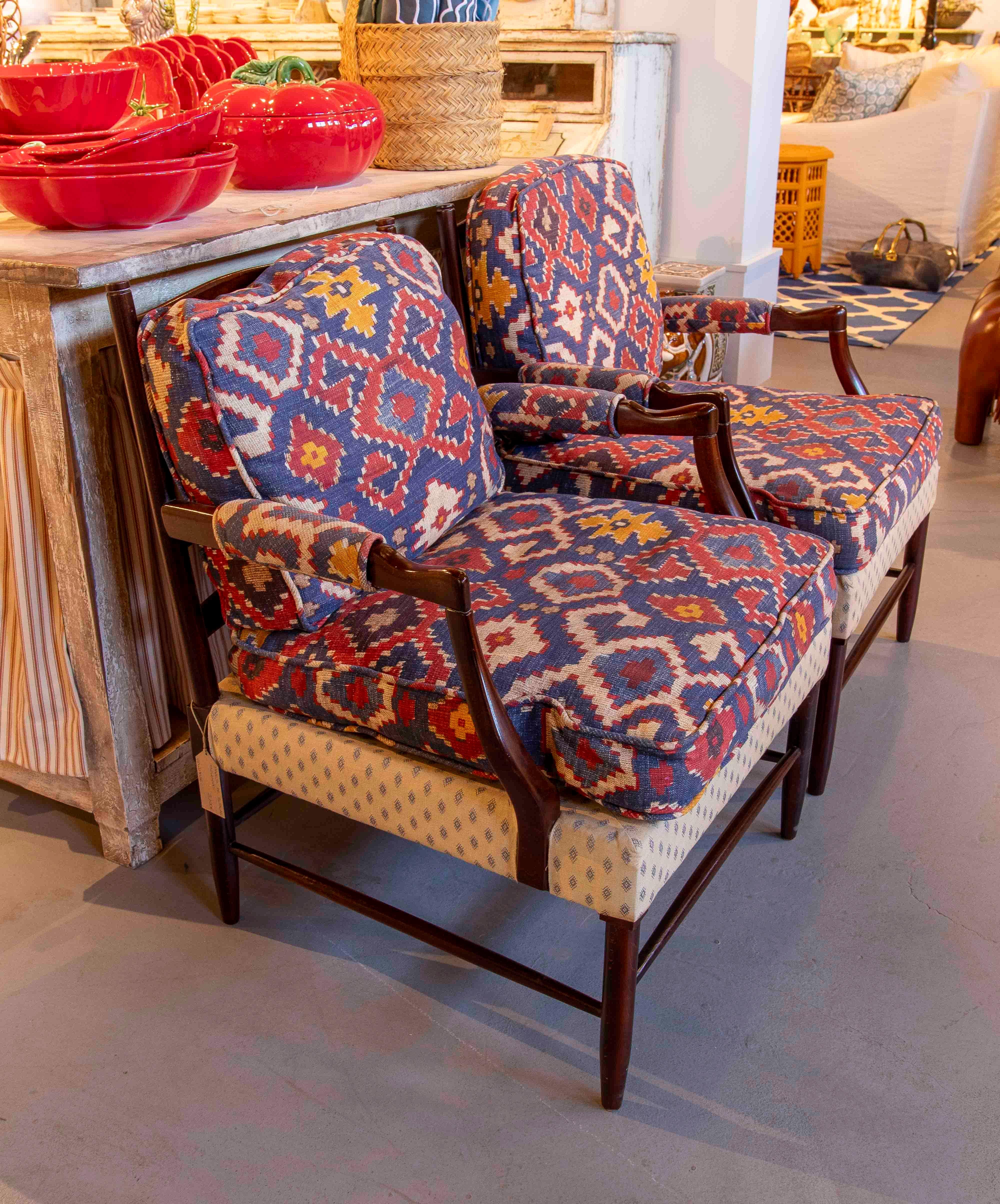 Set of two armchairs with a classic varnished wood frame, updated with vibrant ethnic-inspired Ikat upholstery in shades of blue, red, yellow, and white. The padded seat and backrest offer great comfort, while the upholstered armrests provide a cozy