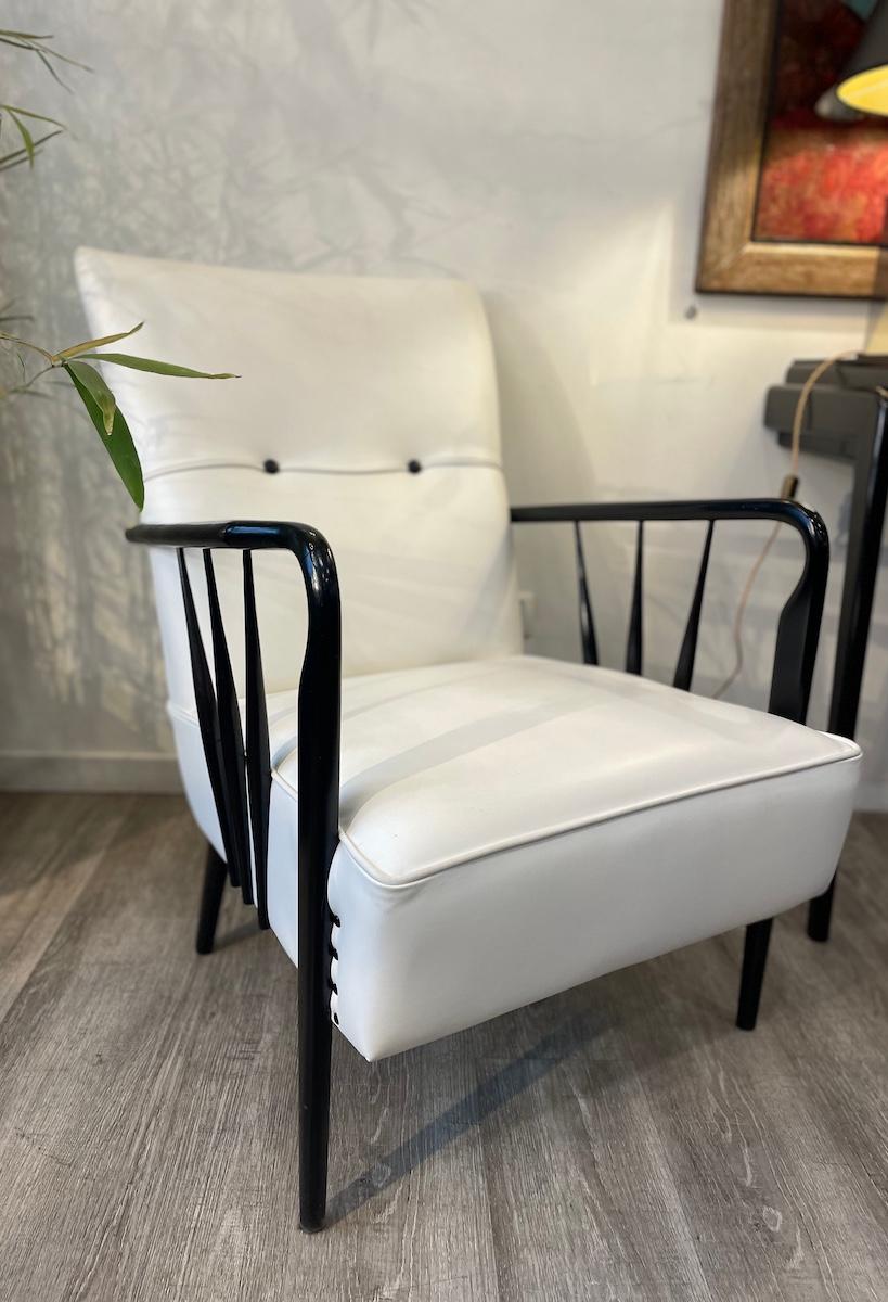 Pair of 1950s armchairs in ebonized wood and white leather. The armchairs are in excellent condition, with a flawless wooden structure. 
The radial design elegantly encloses the cushions. The leather is secured to the seat and backrest with black