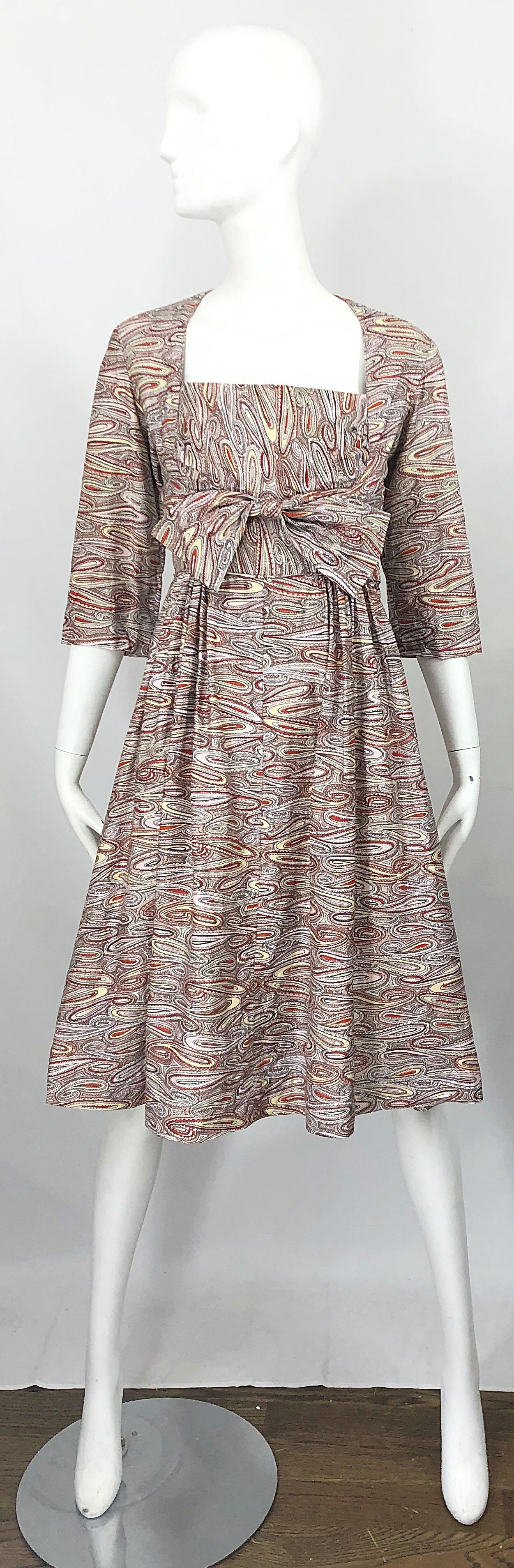 Chic 1950s paisley fit n' flare cotton dress! Features ivory background with warm hues of maroon, orange, pale yellow nad ivory throughout. Shelf like bust with attached bow. Metal zipper up the side. Very well made, with heavy attention to details.