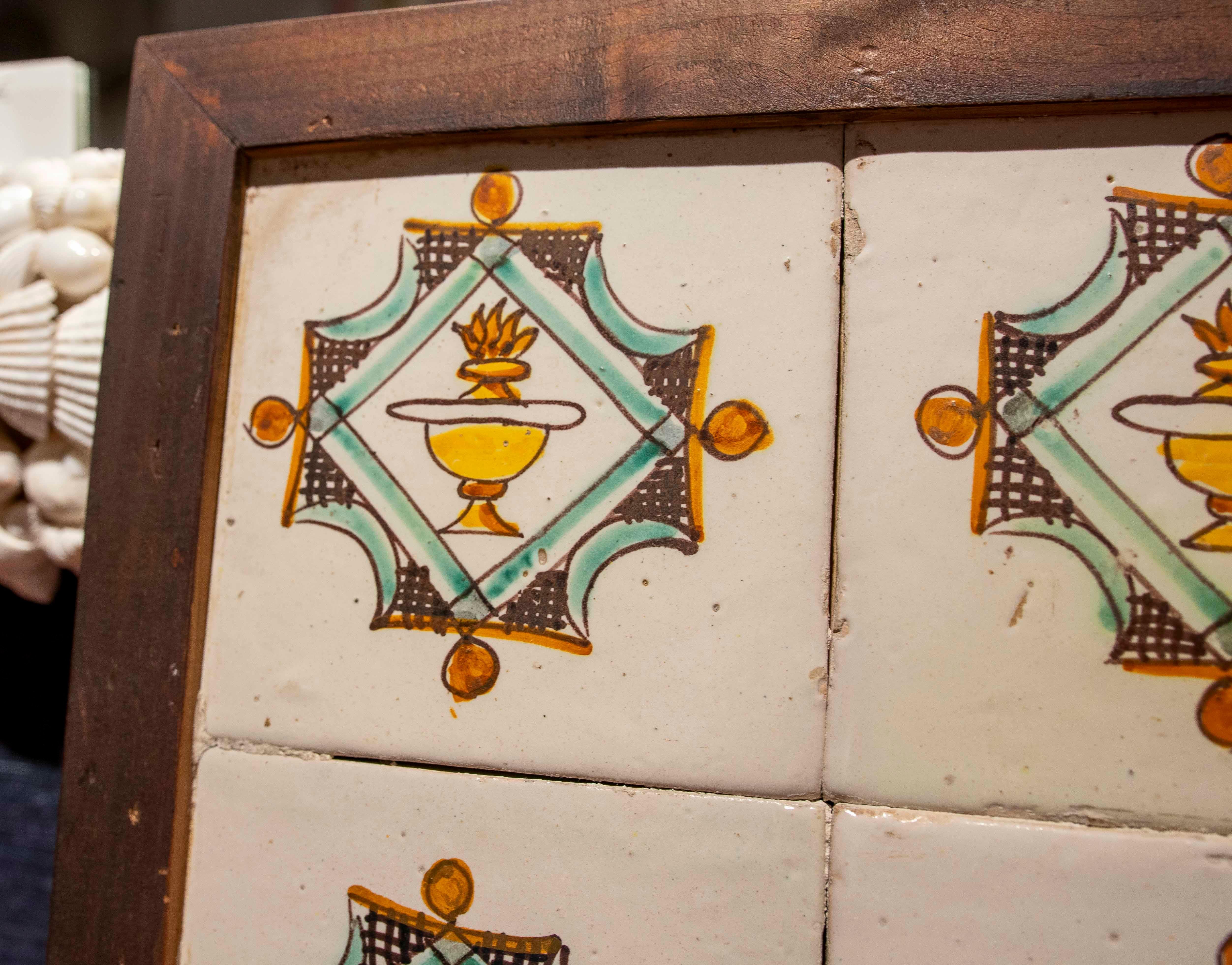 Set di quattro piastrelle antiche incorniciate in legno, decorate con un disegno geometrico e un calice centrale con dettagli nei toni del verde, ocra e nero. La composizione simmetrica e i colori tradizionali evocano lo stile artigianale delle