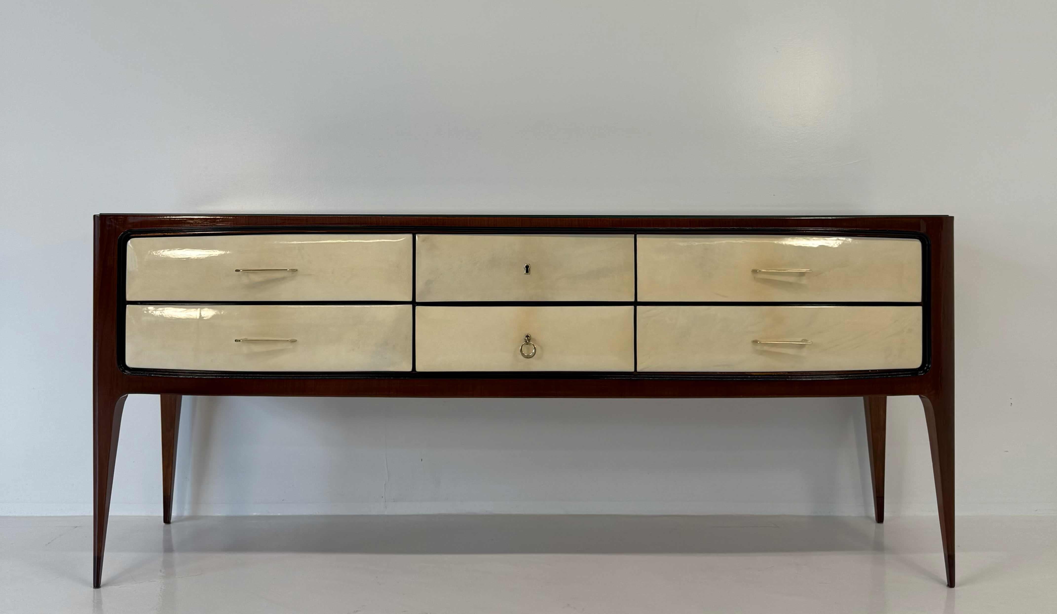Questo comò degli anni '50, attribuito a Paolo Buffa, è stato realizzato in Italia in noce con i frontali dei cassetti in pregiata pelle di pergamena. 
Profili in legno ebanizzato e piano in vetro nero.
Maniglie e chiavi in ottone.

Completamente