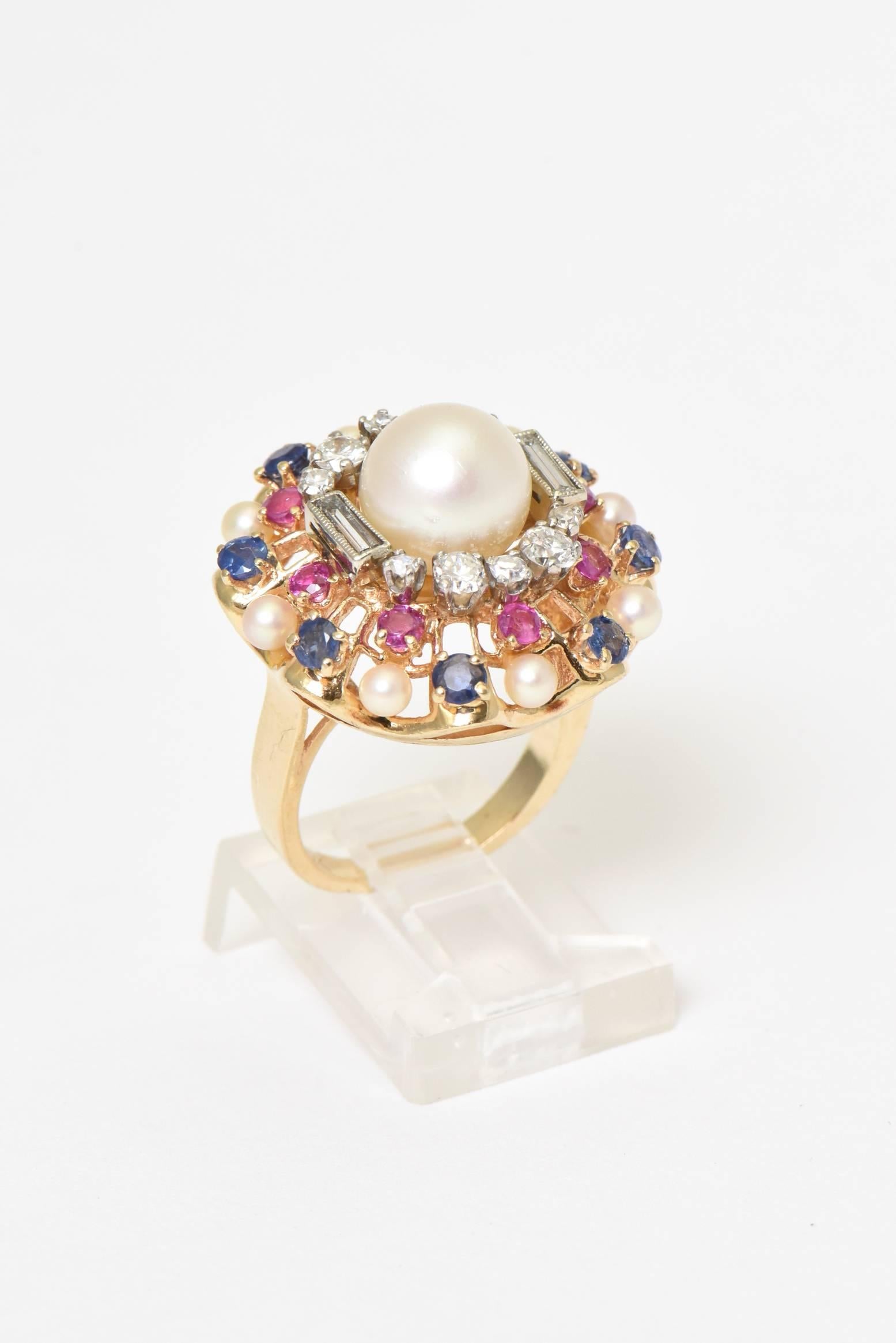 Finely made 14k yellow gold cocktail ring featuring a 8.92mm cultured pearl centrally set in a round and baguette white gold diamond frame within a scalloped frame of rubies, sapphires and tiny pearls.
Marked 14k
Ring Size: 5