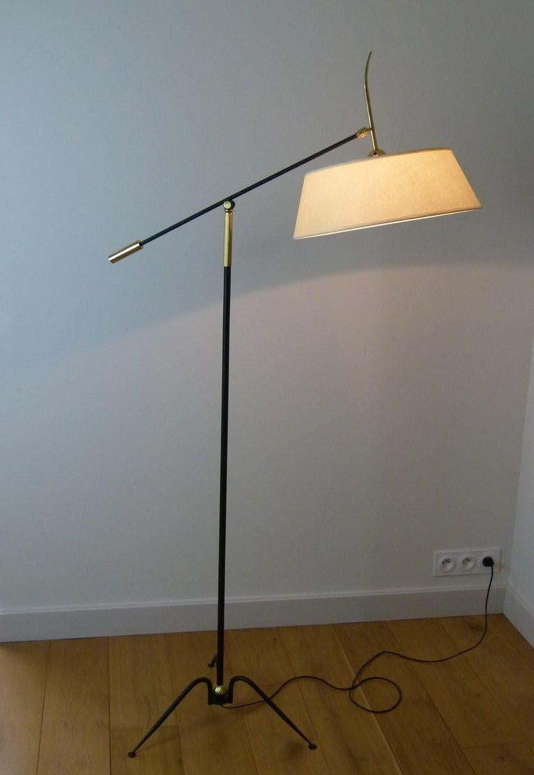 Floor lamp with pendulum and ball joint in brass and black lacquered metal composed of a tripod foot decorated with a brass ring. Black lacquered metal finished with a brass adjusting handle used to tilt the arm of light.
A round and slightly
