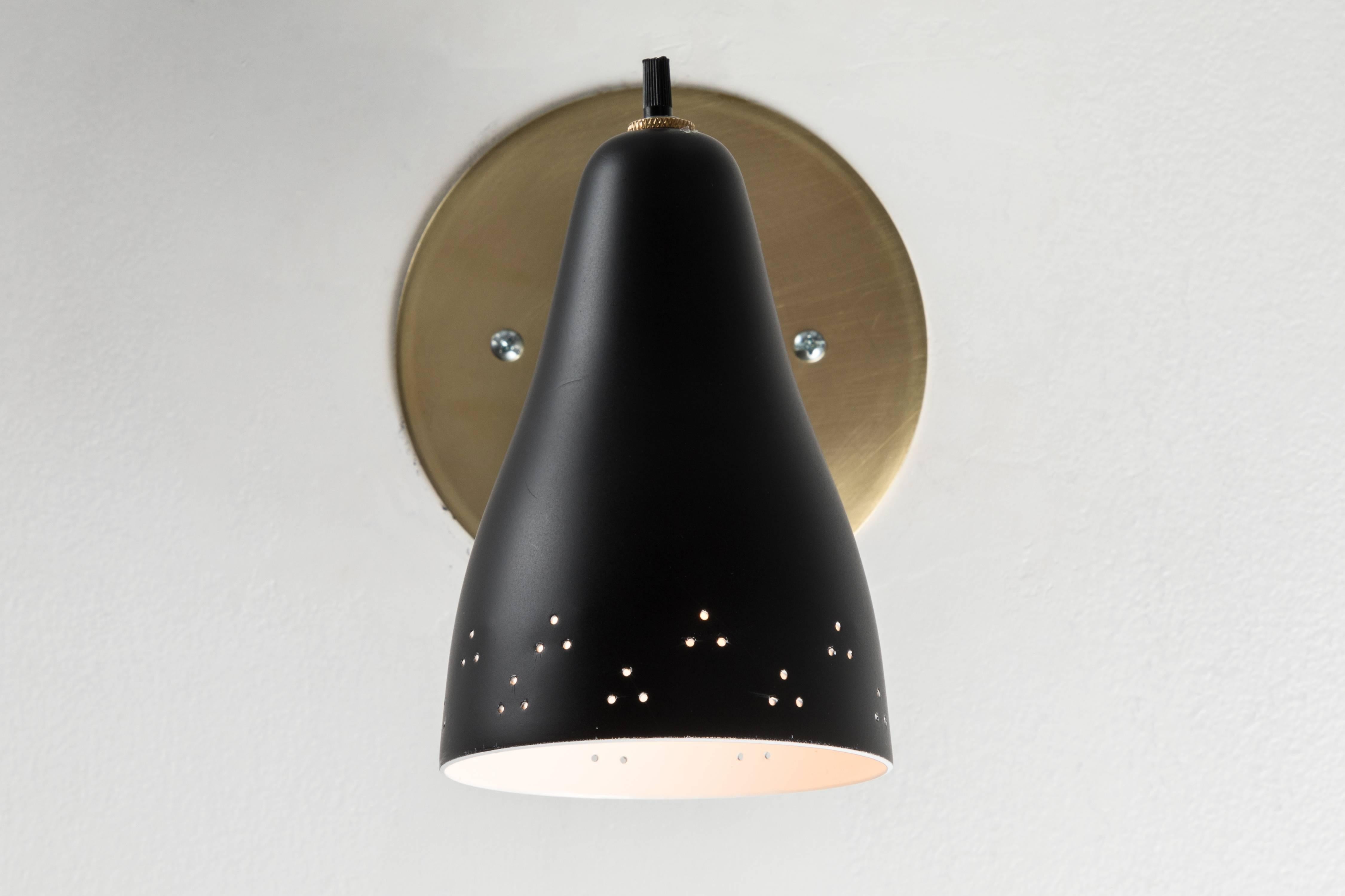 1950s perforated Italian sconce in the manner of Giuseppe Ostuni. Executed in brass and black painted perforated aluminium shade. 

NOTE: Only one light available.

Wired for US electrical J-boxes. Custom patinated brass backplates. Each sconce
