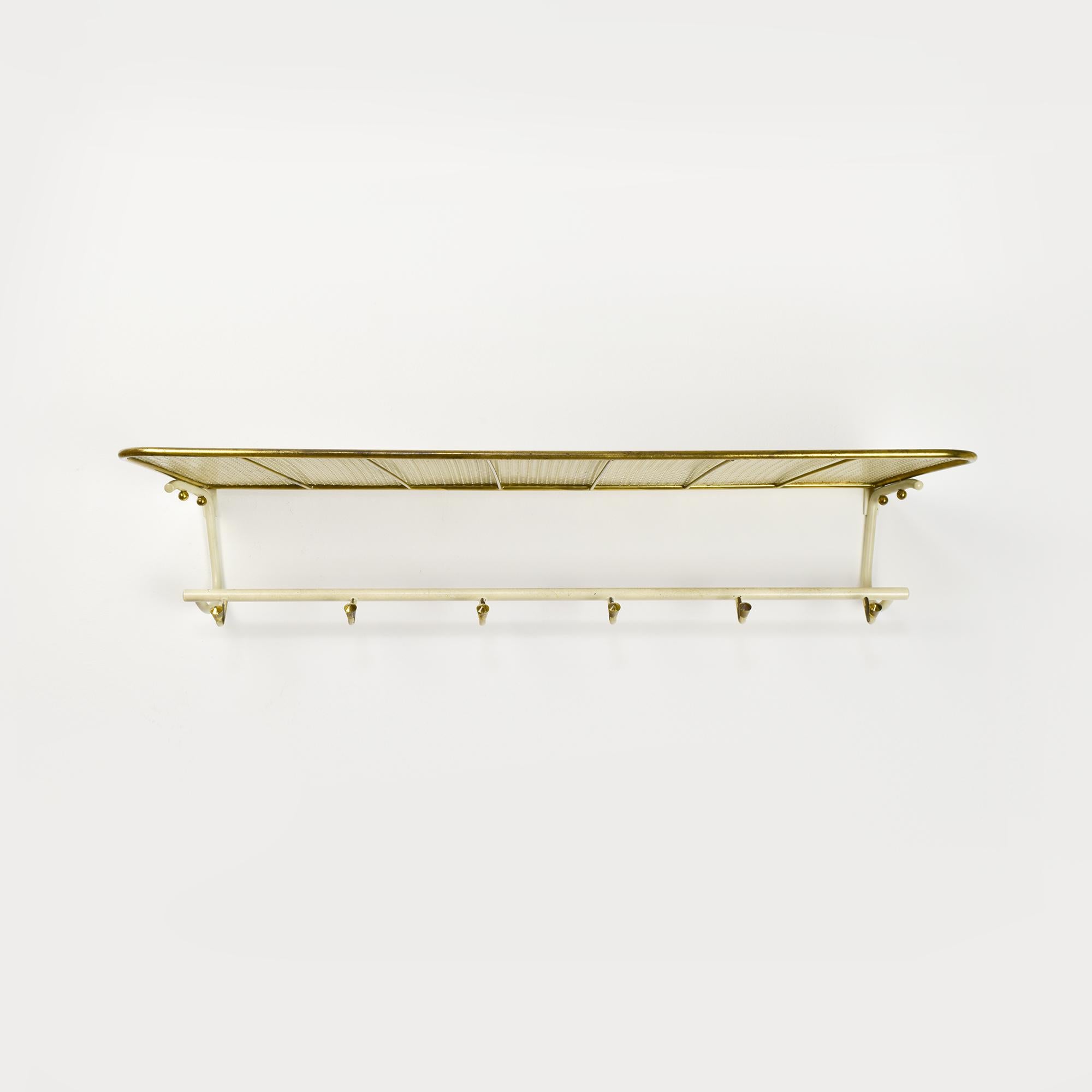 Questo appendiabiti vintage degli anni '50 sfoggia un design unico realizzato in metallo traforato, con eleganti accenti in ottone. La forma distintiva dell'appendiabiti è caratterizzata da una parte superiore ampia e arrotondata che funge da