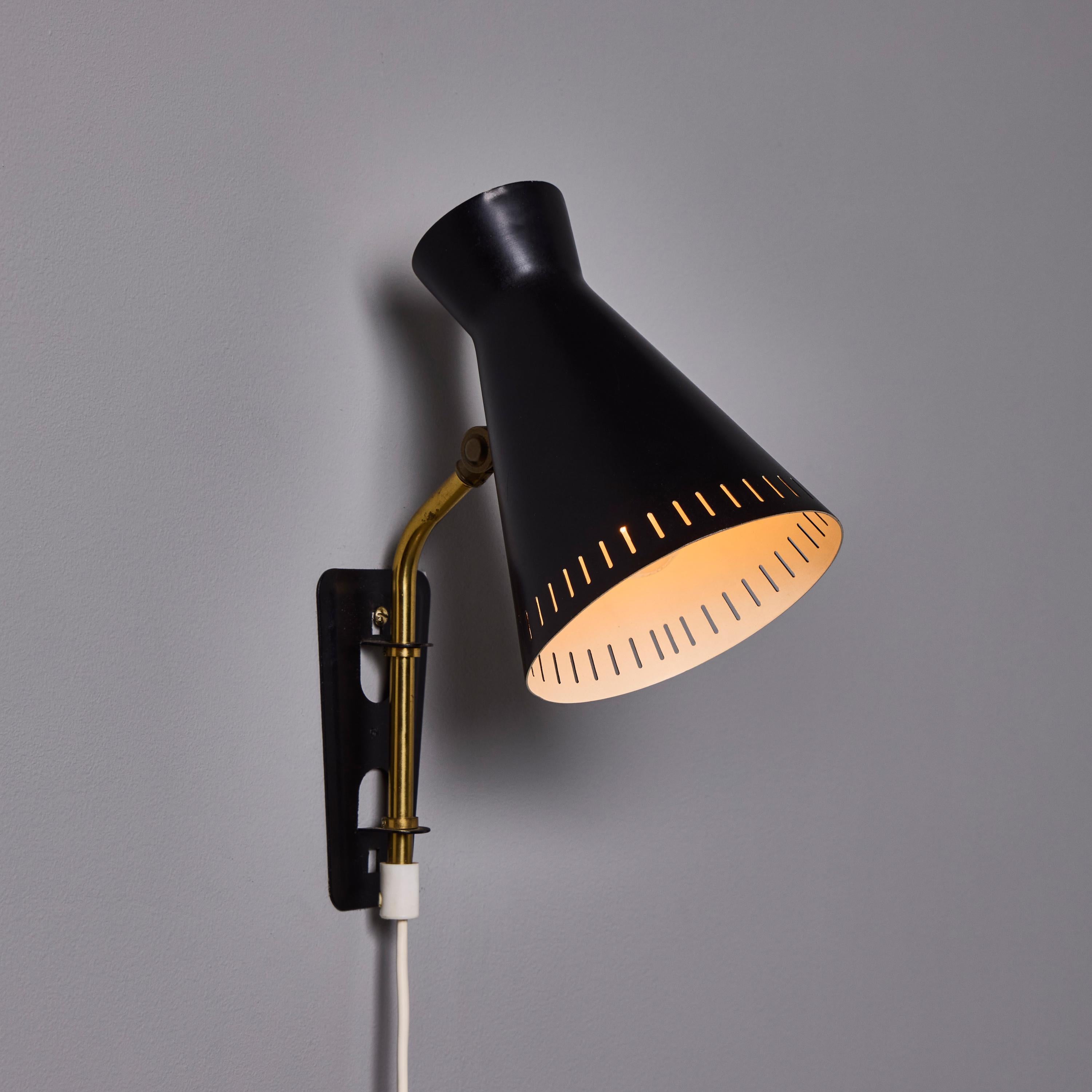 1950s Perforated Metal Diabolo Plug-In Wall Lamp Attributed to Mauri Almari. 

A rare and elegant design executed in sculptural black painted perforated metal with attractively patinated brass arm. Total fixture height of shade and arm is 9.75