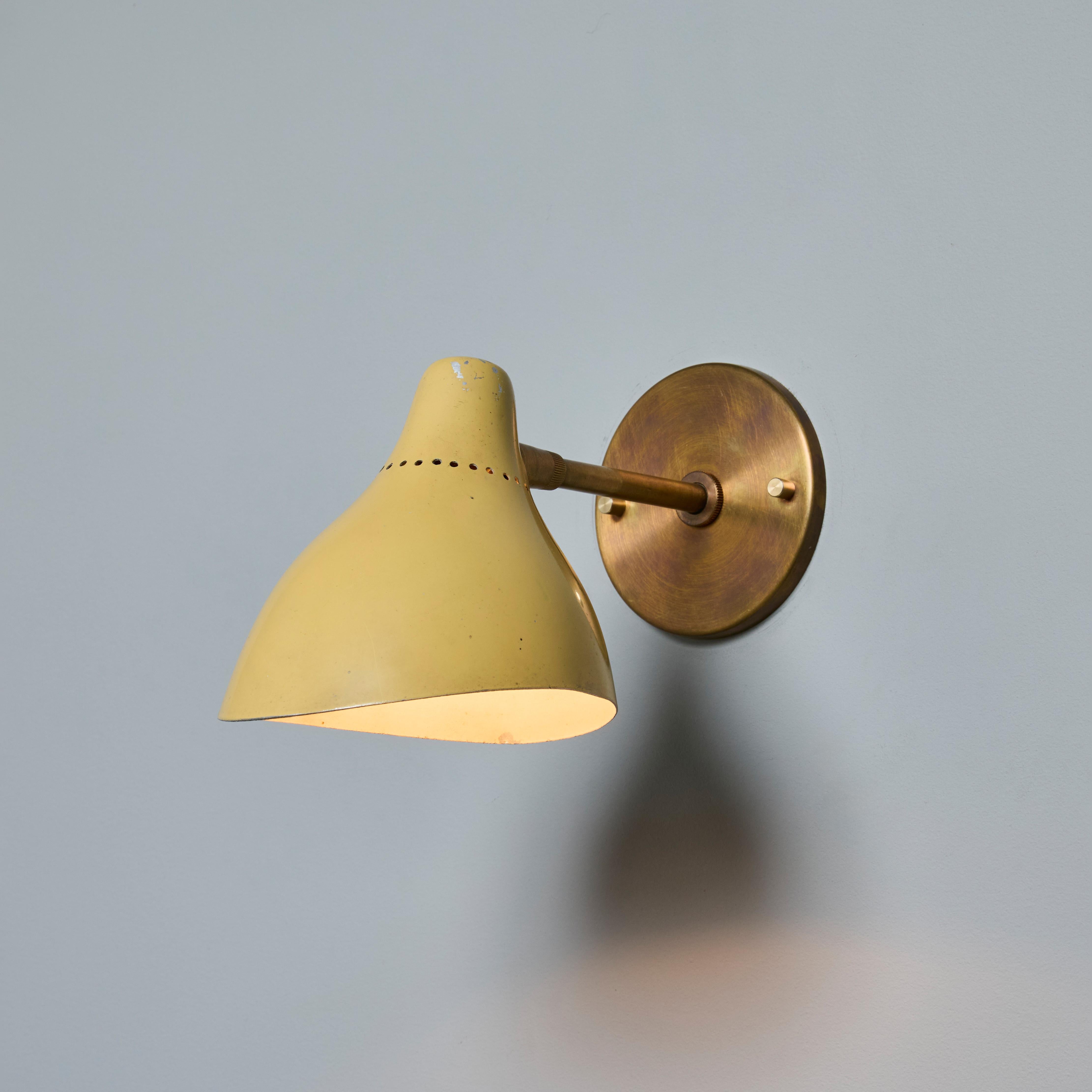 Lampe murale des années 1950 en métal peint perforé et laiton, attribuée à Stilnovo. Abat-jour en métal perforé peint avec bras et plaque arrière en laiton patiné. L'abat-jour pivote librement de gauche à droite et de haut en bas sur une rotule. Un