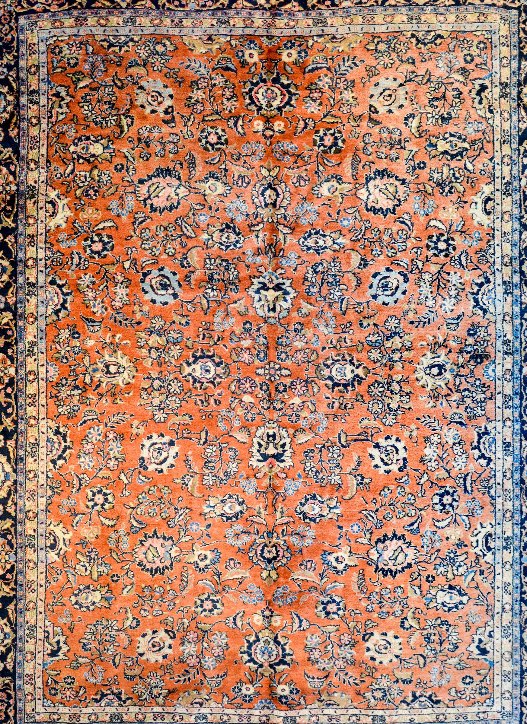 1950s Persian Qazvin rug with an all-over abstract floral pattern woven in light and dark indigo, green, gold, and cream, on a burnt orange colored background. The border is wonderful, with a wide central stripe with a large-scale floral and