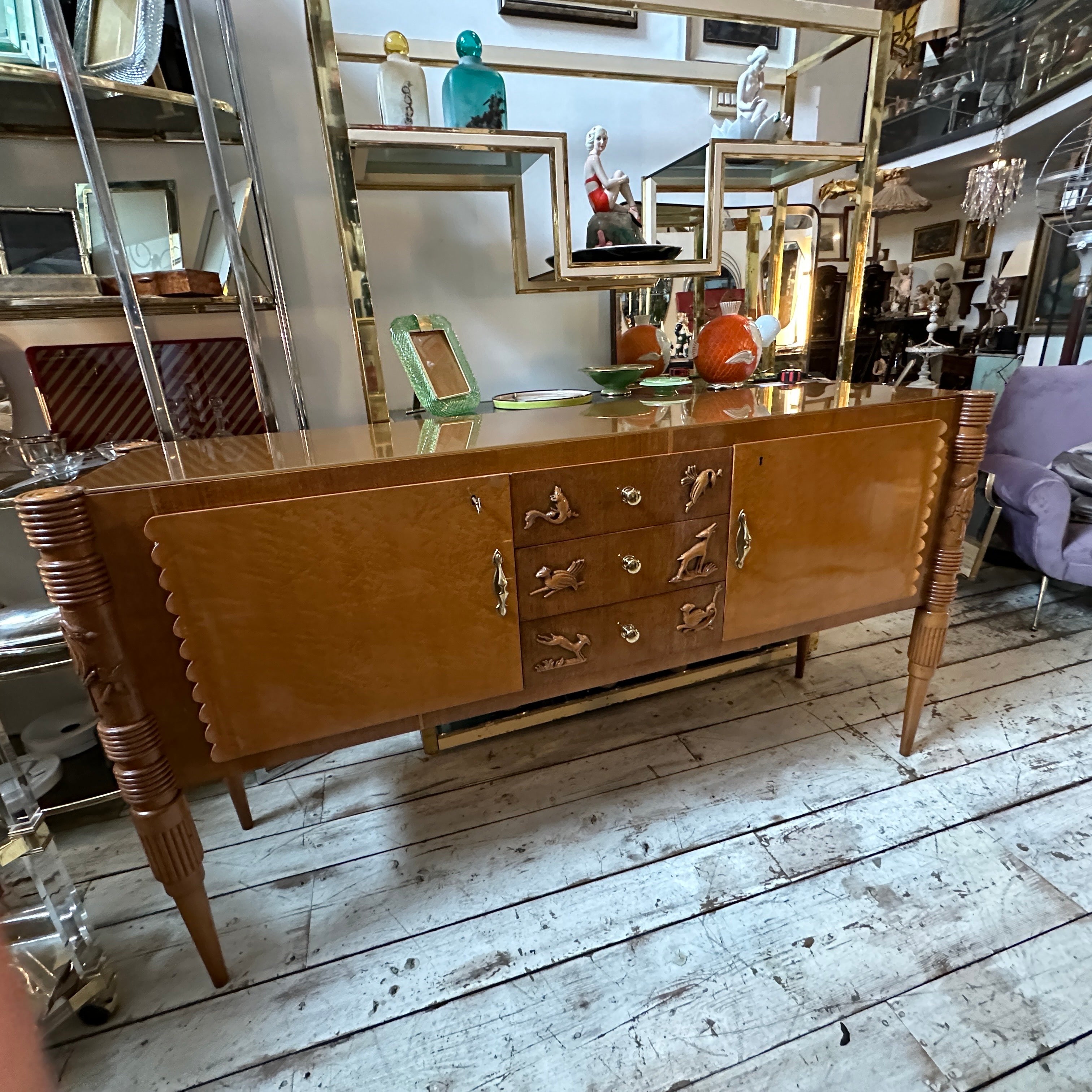 An italian sideboard with a burled birch veneer designed by Pier Luigi Colli and manufactured by F.lli Marelli Cantu.  Two exterior cabinet doors with brass door handles, centering three drawers with carved bird decorations on the fronts with brass