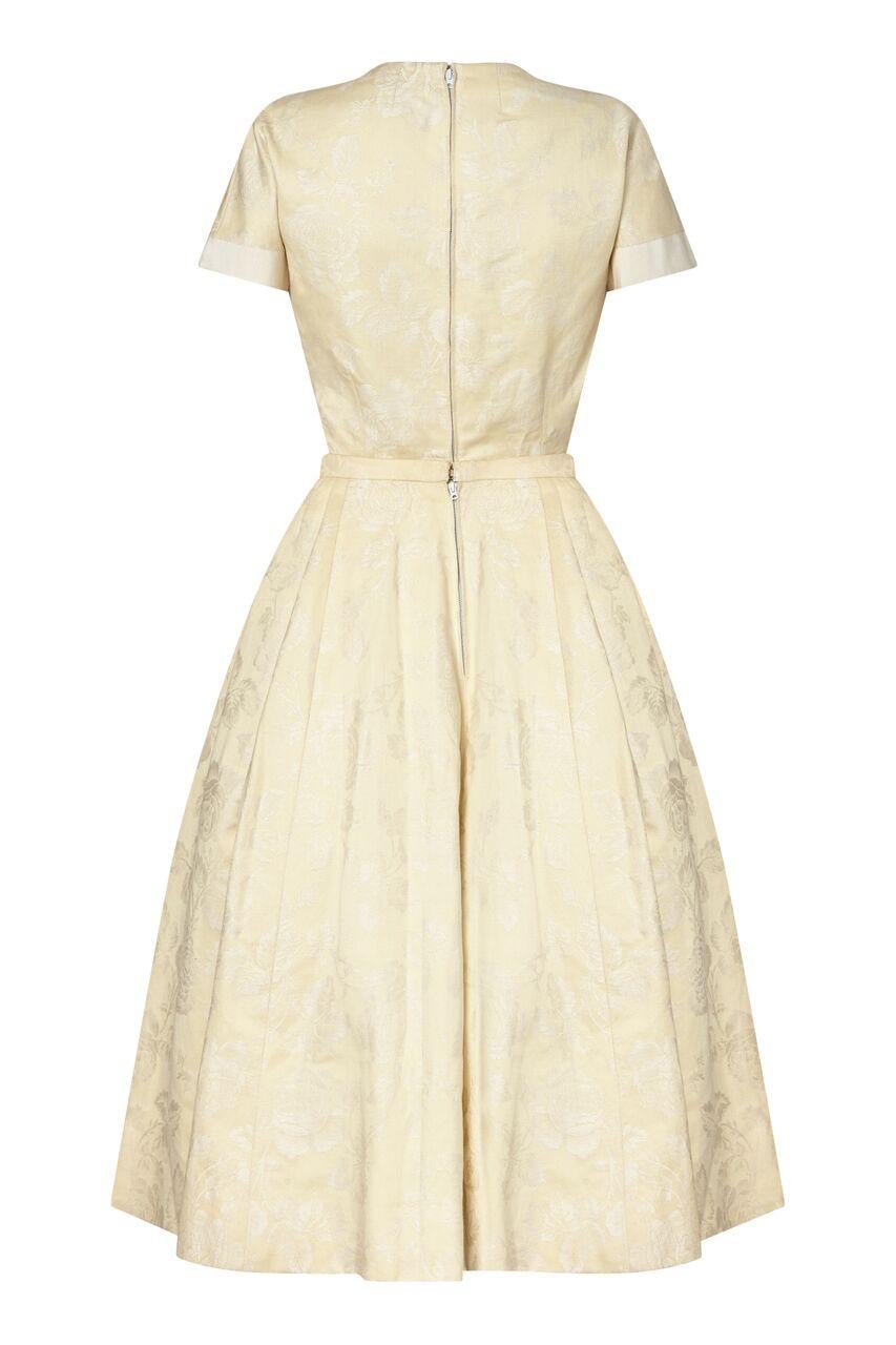 This timeless 1950s New Look style demi couture two piece by Pierre Balmain is in impeccable condition with exceptional line and form. The soft cream jacquard fabric is embossed with a romantic rose design and features wide bands of ivory grosgrain