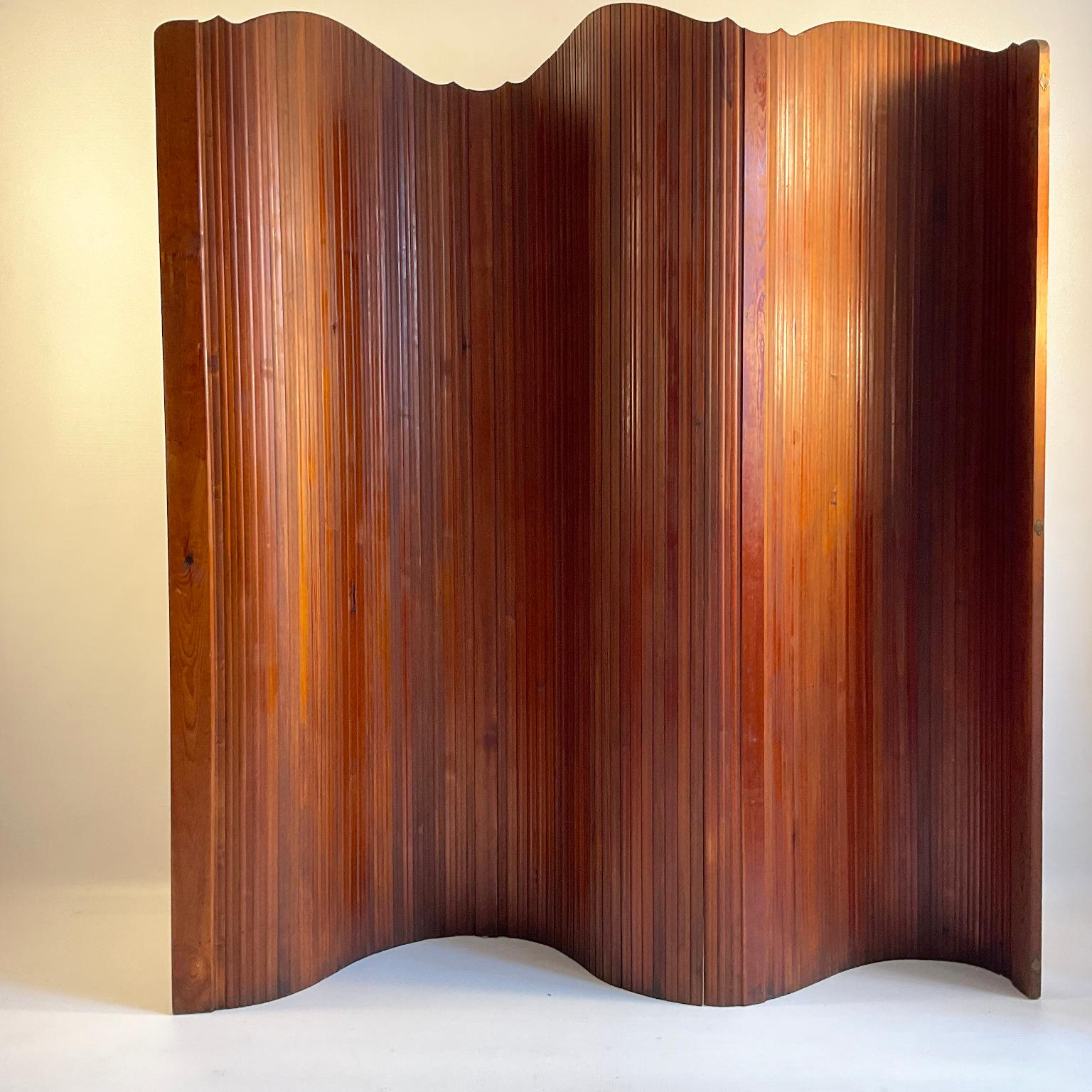 1950s Tambour screen by the French manufacturer S.N.S.A. Made in stained pitchpine.
Its flexible structure allows it to stand freely and shape curves, perfect for a dressing room or as a room divider, can also be rolled up for easy storage.