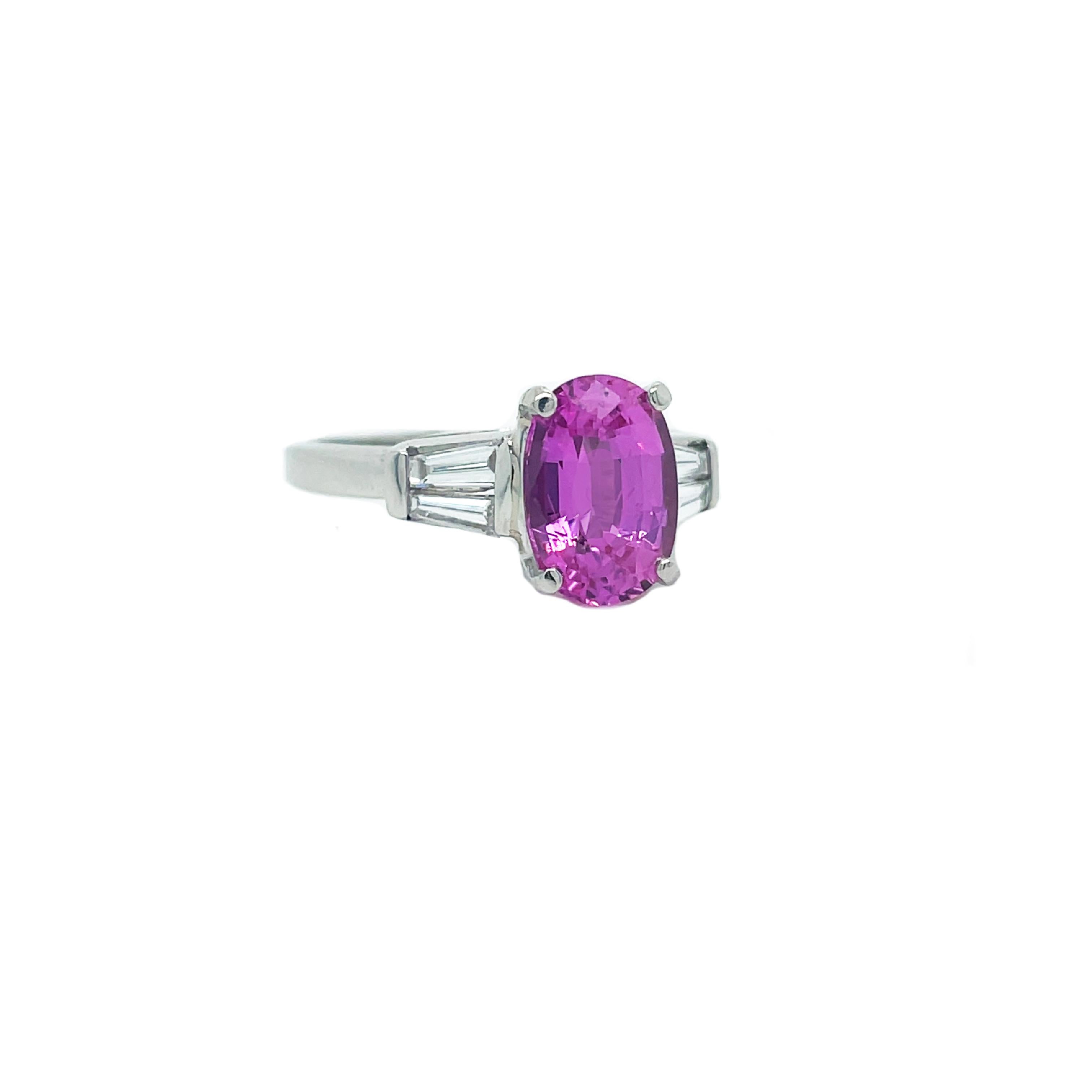 This is a stunning 1950s platinum ring showcasing an exceptional vivid pink sapphire with baguette shoulders! In this truly incredible and outstanding jewel, a 2.17-carat oval sapphire radiates a luscious, vivid and playful pink between a pair of