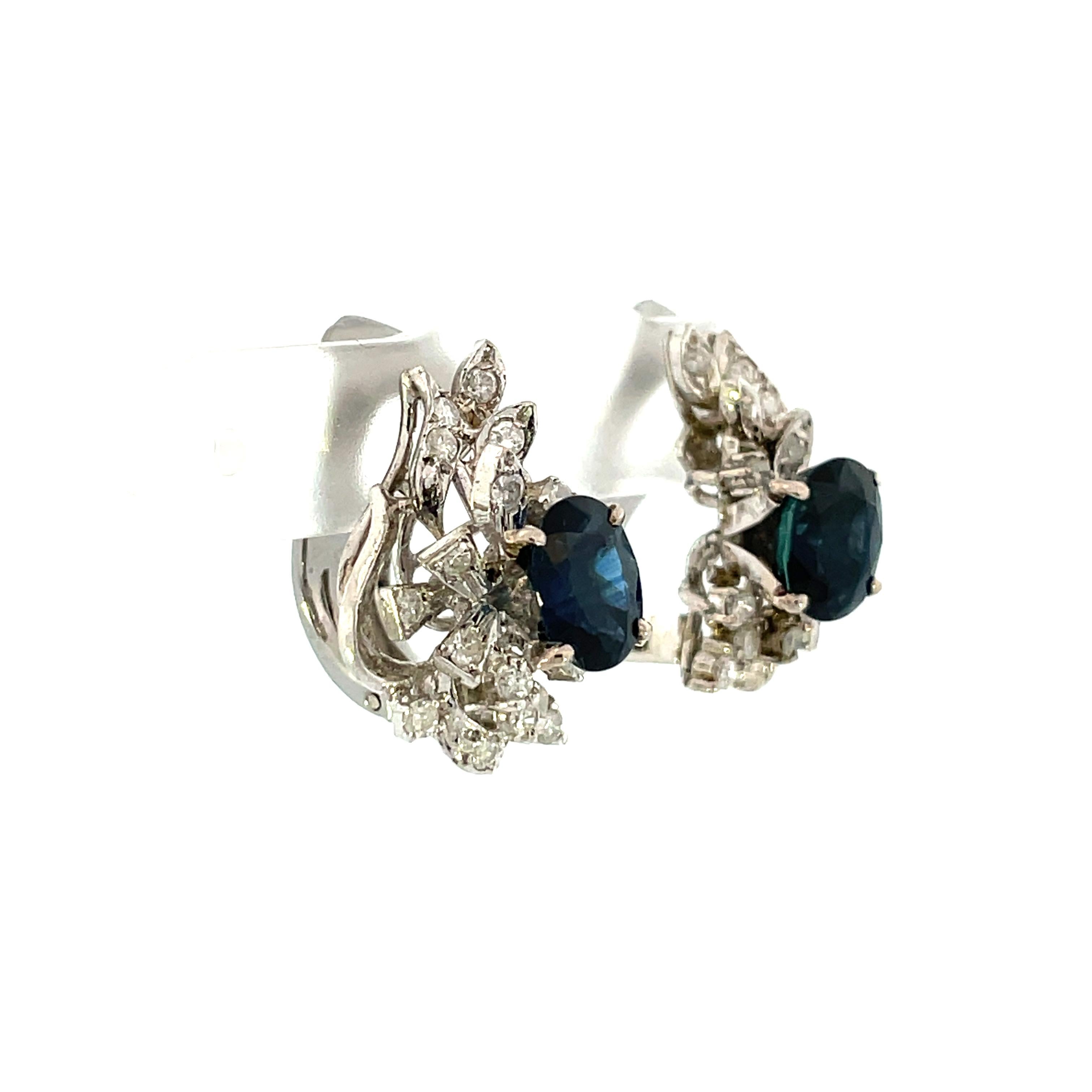This midway retro pair of 1950s platinum and diamond earrings starring medium blue sapphires provide a secure and comfortable fit for those without pierced ears. This pair includes .32 tw of G color SI1 clarity diamonds, multi-layered within the