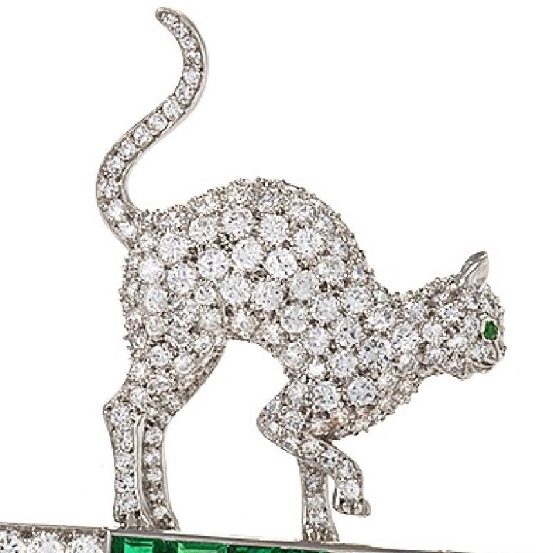 A Mid-20th Century brooch with diamonds and emeralds. This charming brooch features an emerald-eyed, diamond crusted cat balanced on the emerald shank of an ornate key. The piece has 220 round-cut diamonds and one baguette, with an approximate total