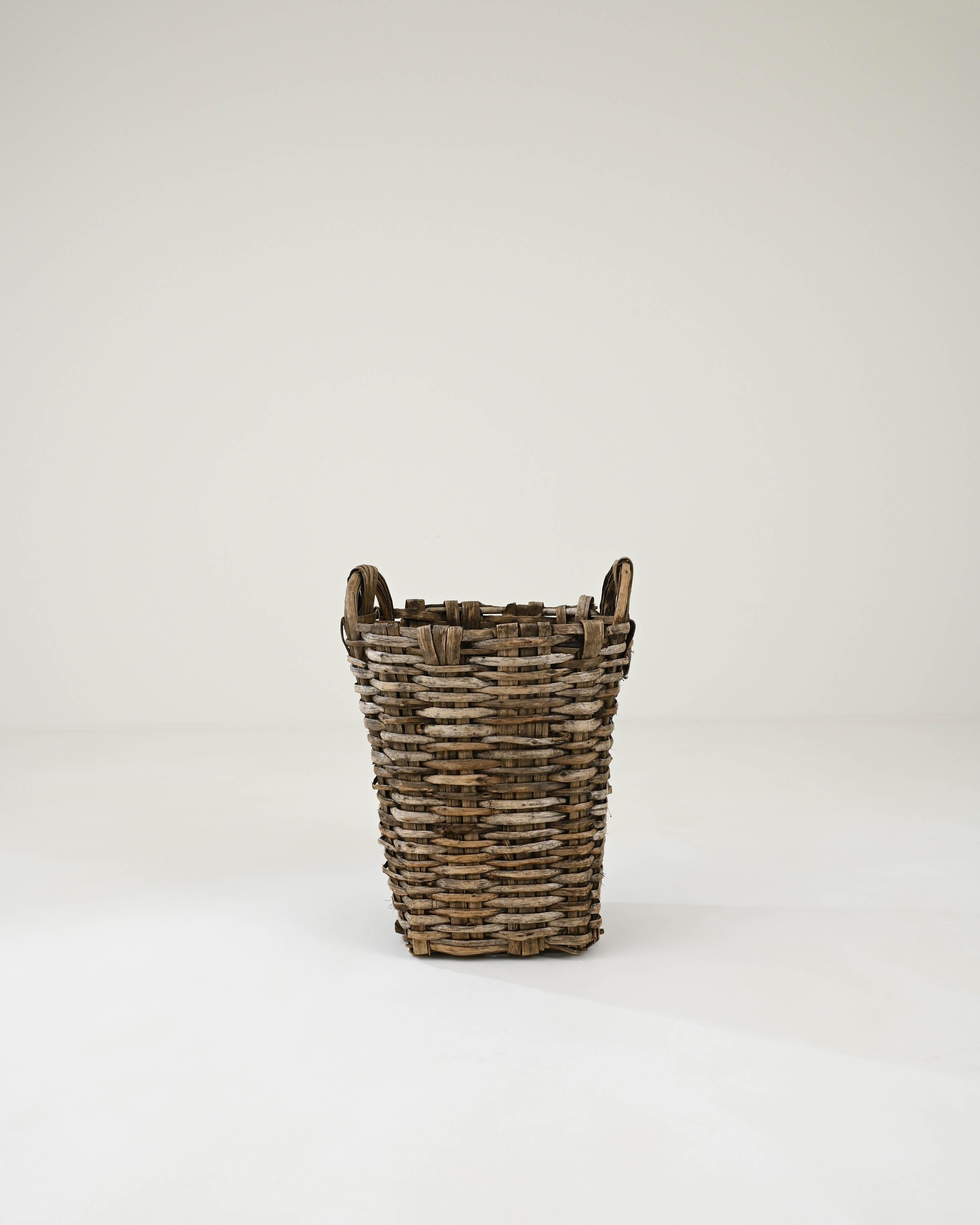 Hand-woven in the 1950s, this artisanal basket exemplifies the rich tradition of wicker basketry in Portugal that dates back centuries. The masterful weaving technique features captivating patterns accentuated by the interplay of natural wicker hues